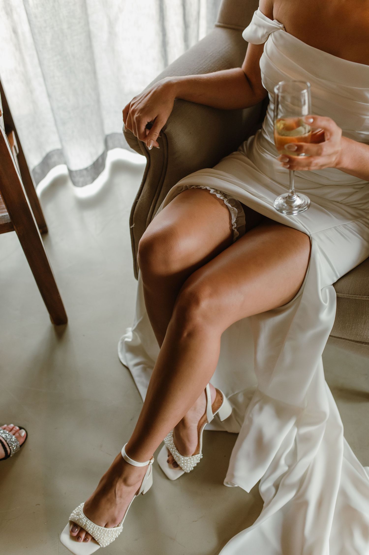 Detail shots of white sandals and flowing dress fabric against a brown chair.