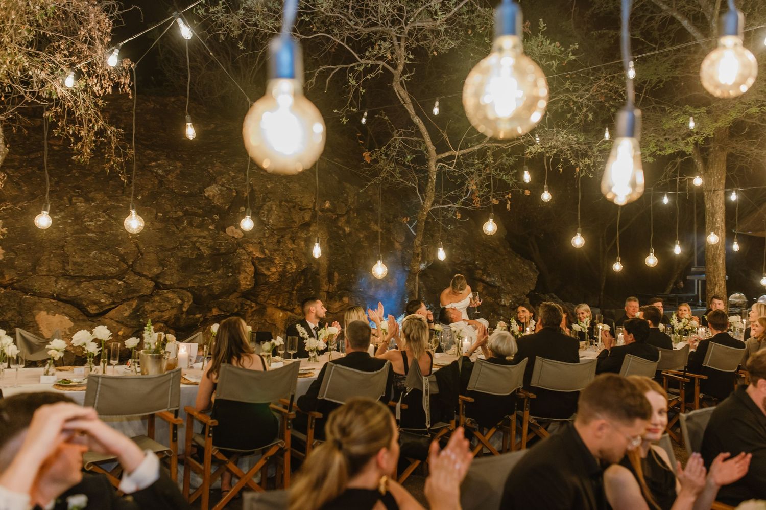 Wedding guests dancing and celebrating under romantic string lights at an outdoor evening reception.