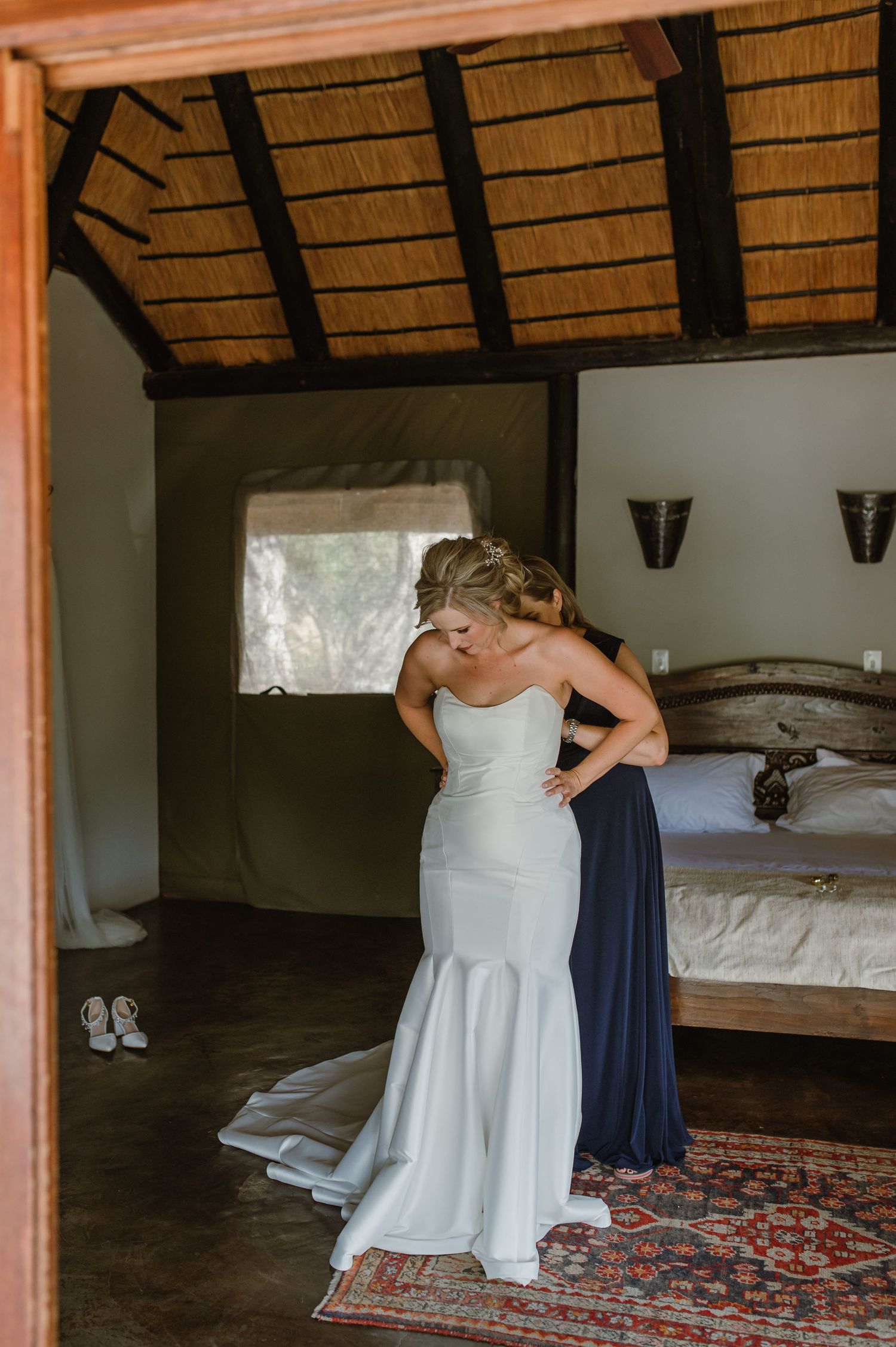 Wedding dress preparation in a rustic room with thatched roof and wooden beams.