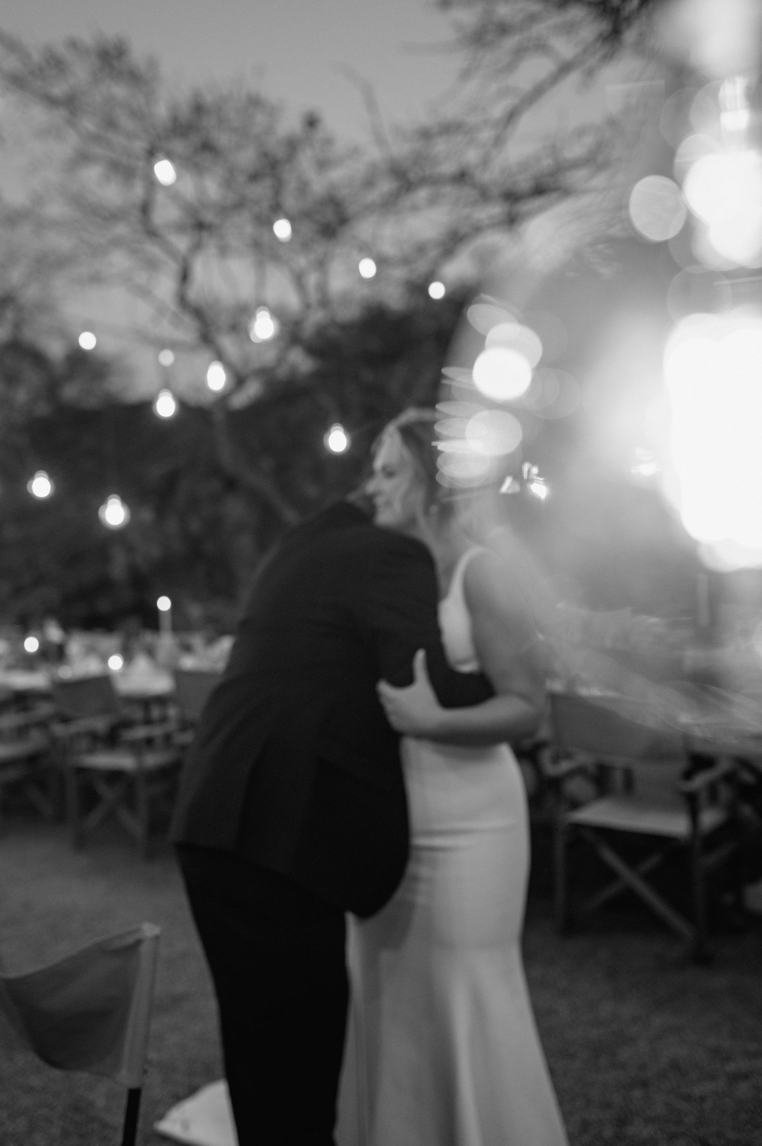Black and white photo of a couple dancing at a rustic outdoor reception.