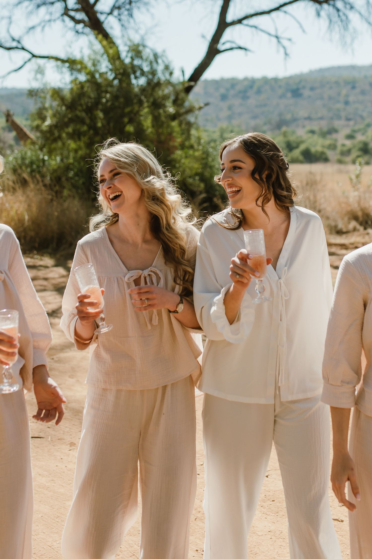 A candid moment shows a line of people in white dresses laughing together outdoors.