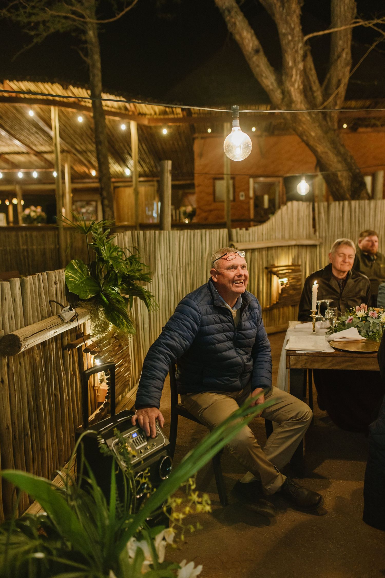Guests relaxing in a rustic outdoor lounge area with string lights and bamboo walls.