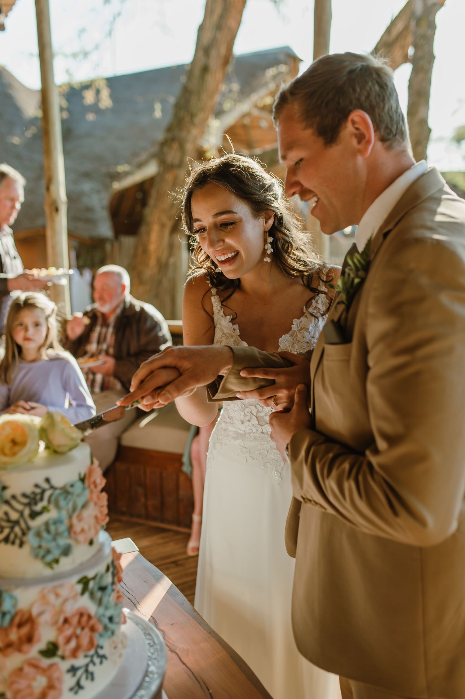 Wedding cake cutting ceremony in a rustic venue with natural lighting and floral decorations.