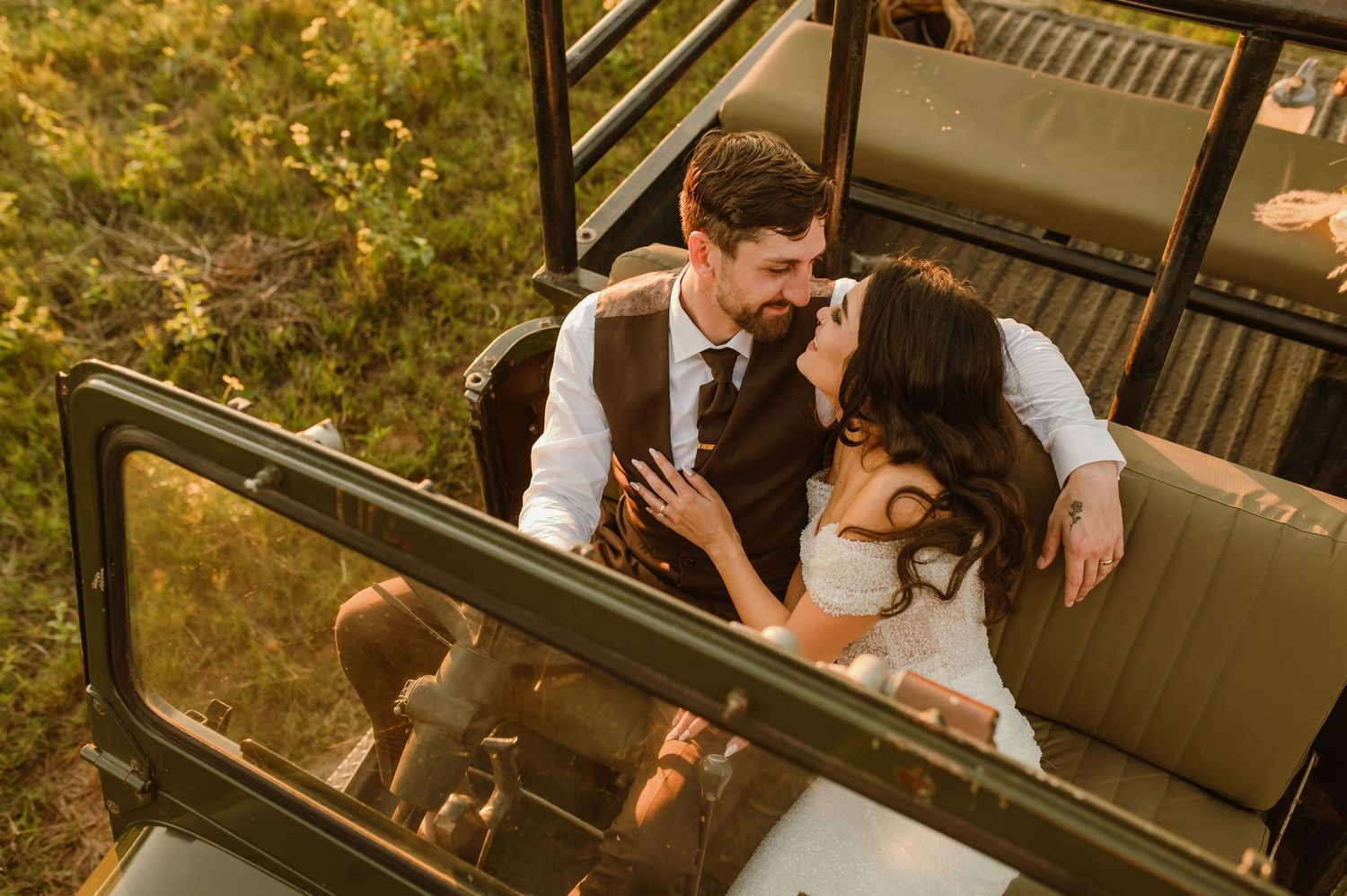 A couple shares an intimate moment in a vintage safari vehicle during sunset.