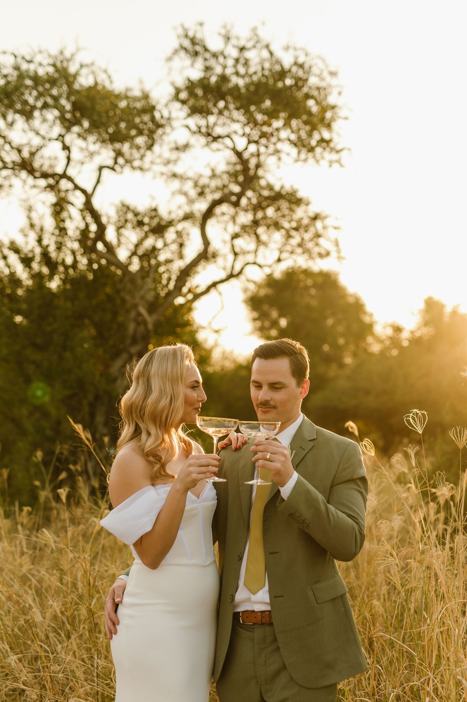 Wedding couple enjoying champagne together in a sunlit field.