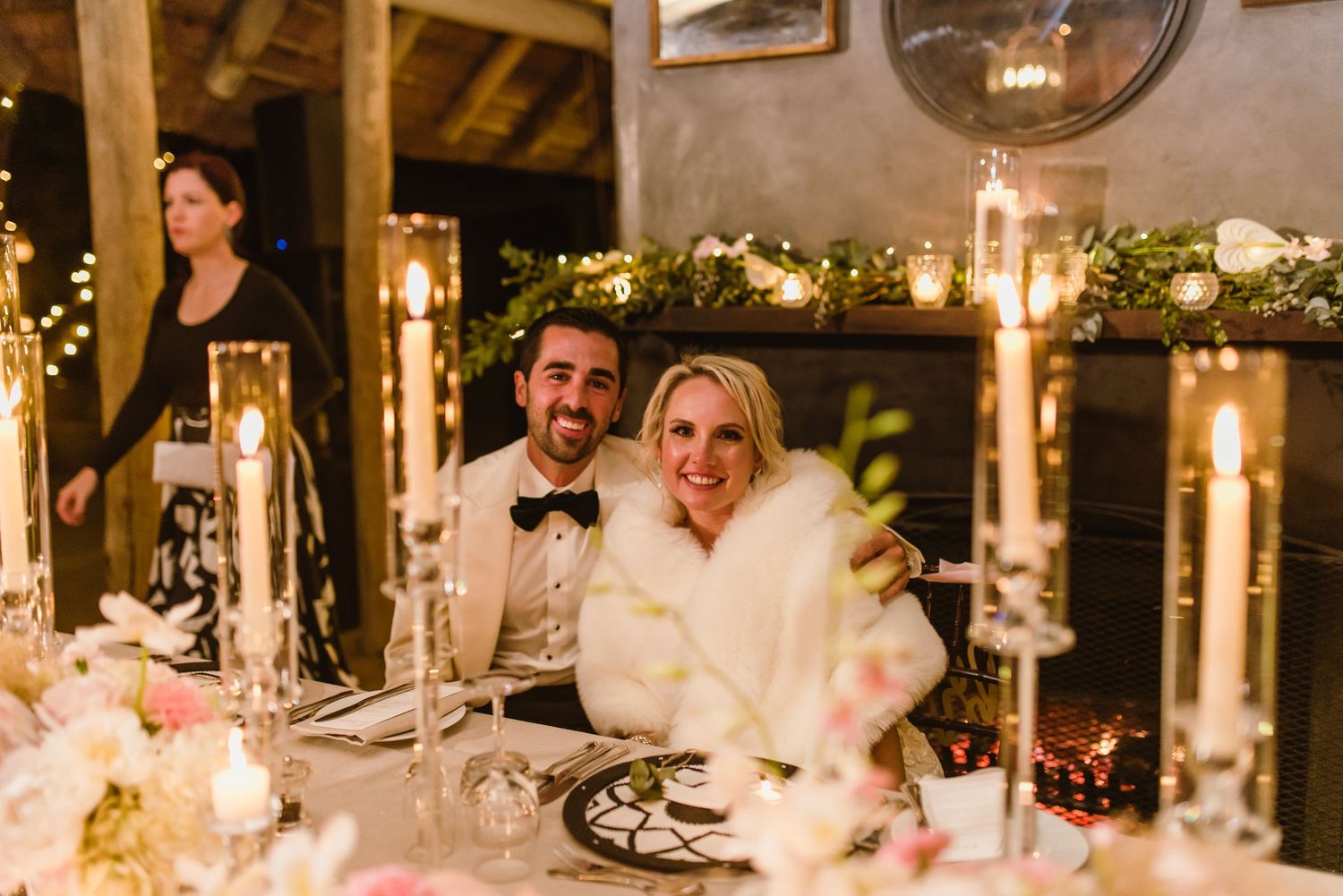Elegant wedding reception dinner table setup with glowing candles and floral centerpieces at dusk.