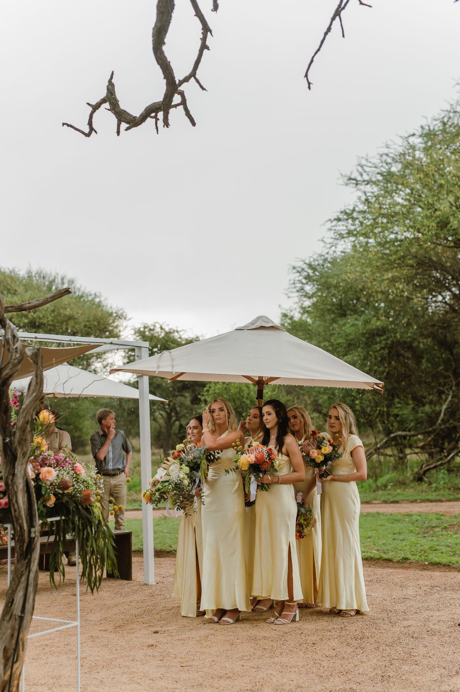 Bridesmaids in light-colored dresses holding bouquets at outdoor desert wedding.