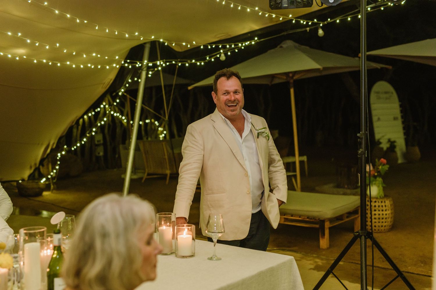 Wedding reception tables decorated with string lights and floral centerpieces in an elegant tent setting.
