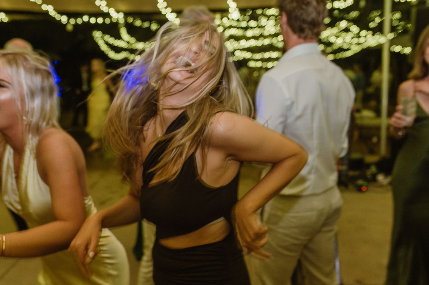 Guests dancing and celebrating at a wedding reception under decorative string light canopy.