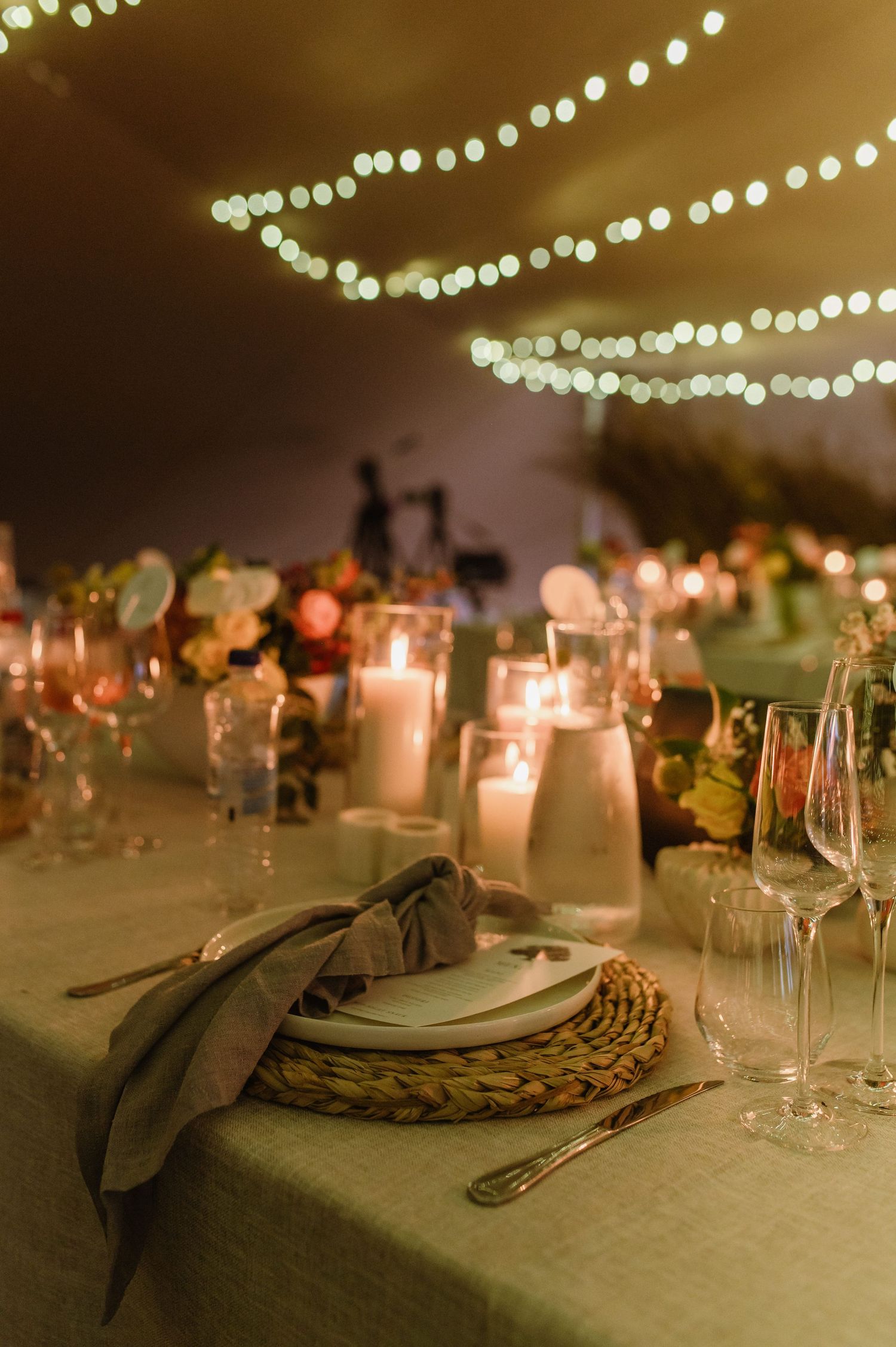 Elegant table setting with string lights overhead and candlelit place settings.