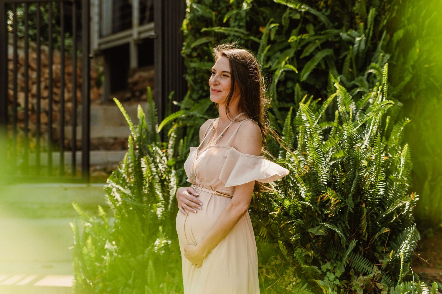 A person in a white summer dress poses in a lush garden setting with natural sunlight filtering through the trees.