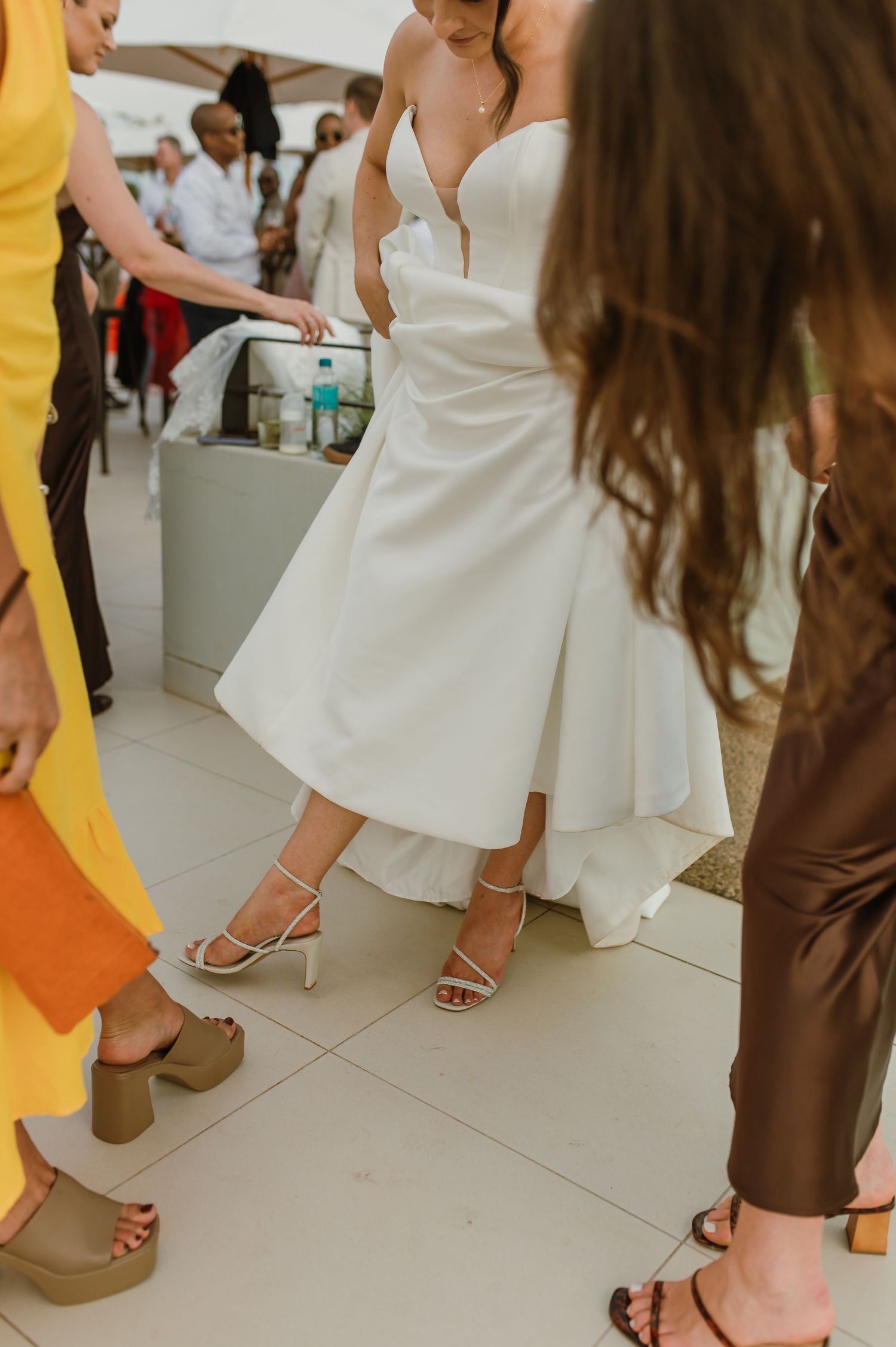 Close-up view of formal event attendees' feet and dresses on a white floor during a celebration.
