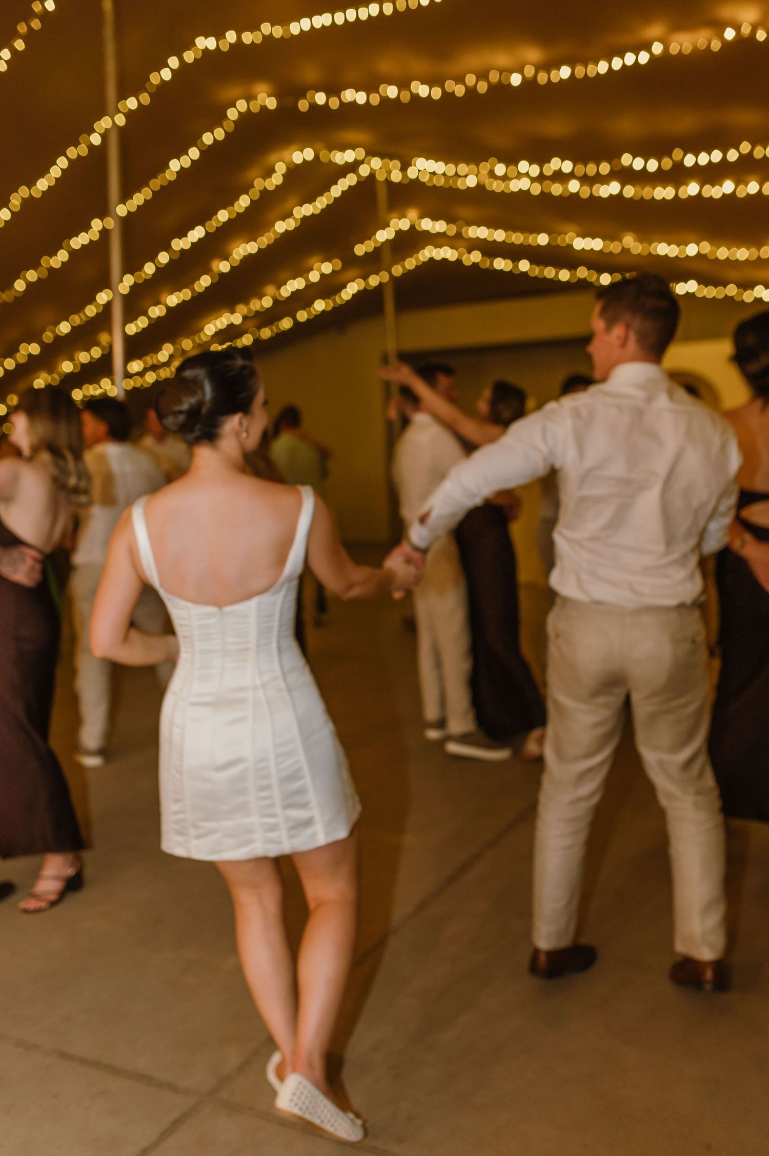 Guests dance under crisscrossing string lights at an evening wedding reception.