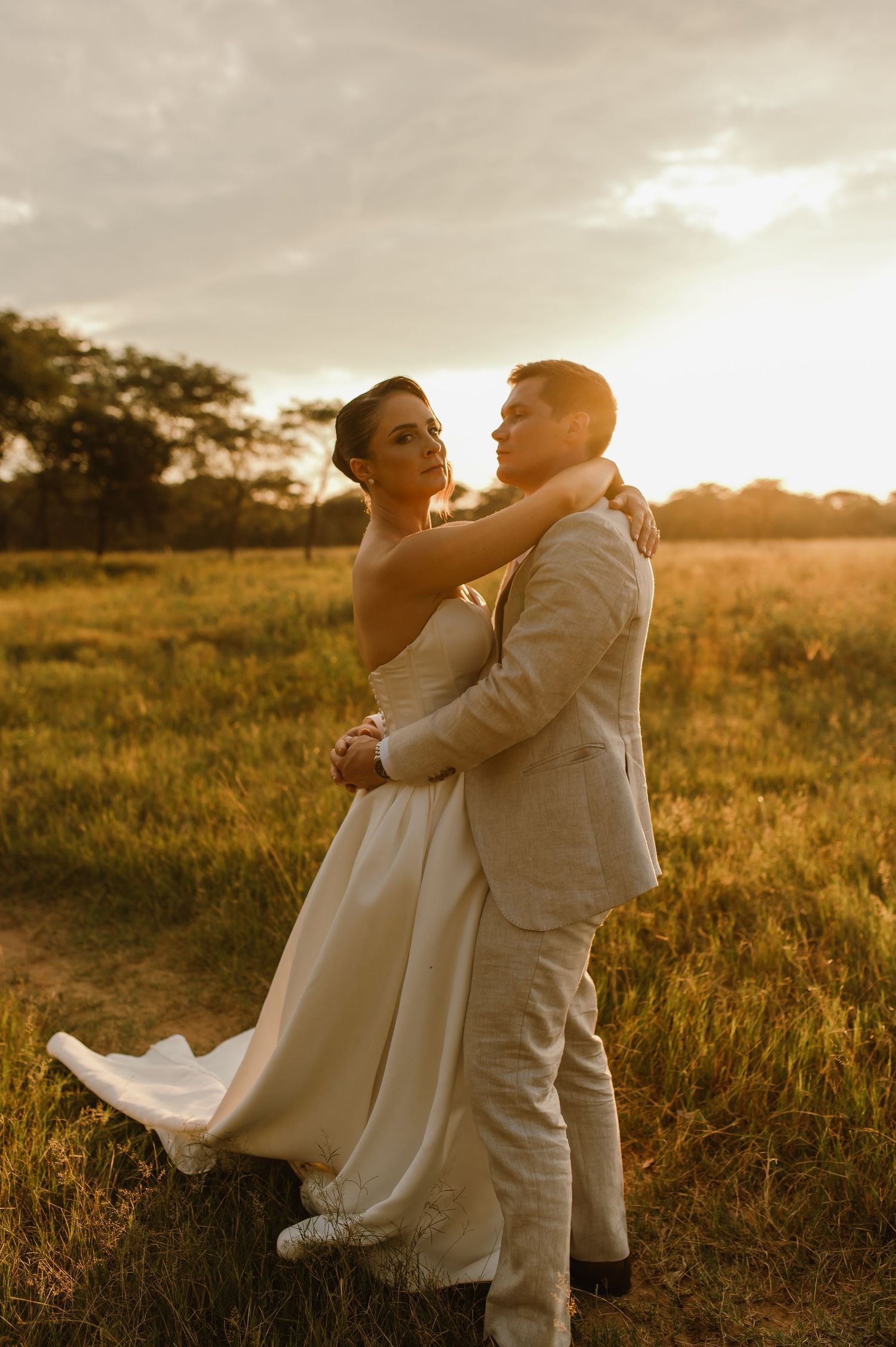 A romantic sunset wedding photoshoot in a golden field with a couple embracing in elegant white attire.