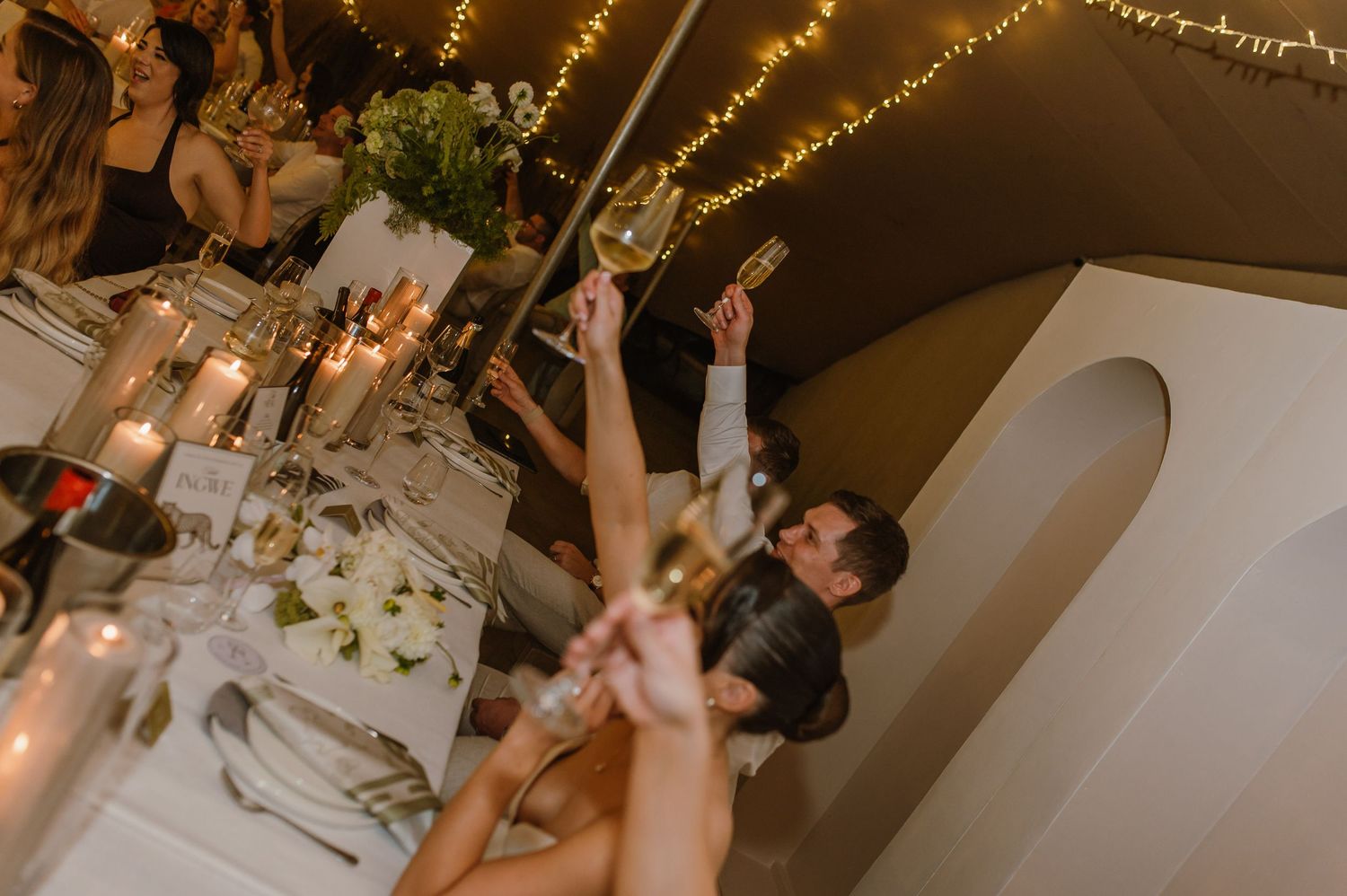 Festive wedding reception with string lights illuminating tables and dancing guests.