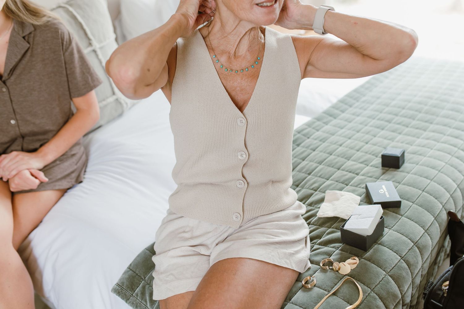 Woman in cream-colored romper sitting on green cushioned outdoor furniture.