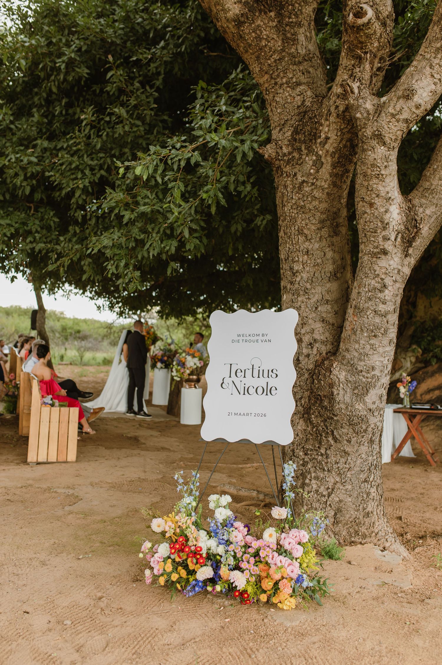 Wedding welcome sign for Tertius and Nicole displayed on an easel with colorful flowers at base.