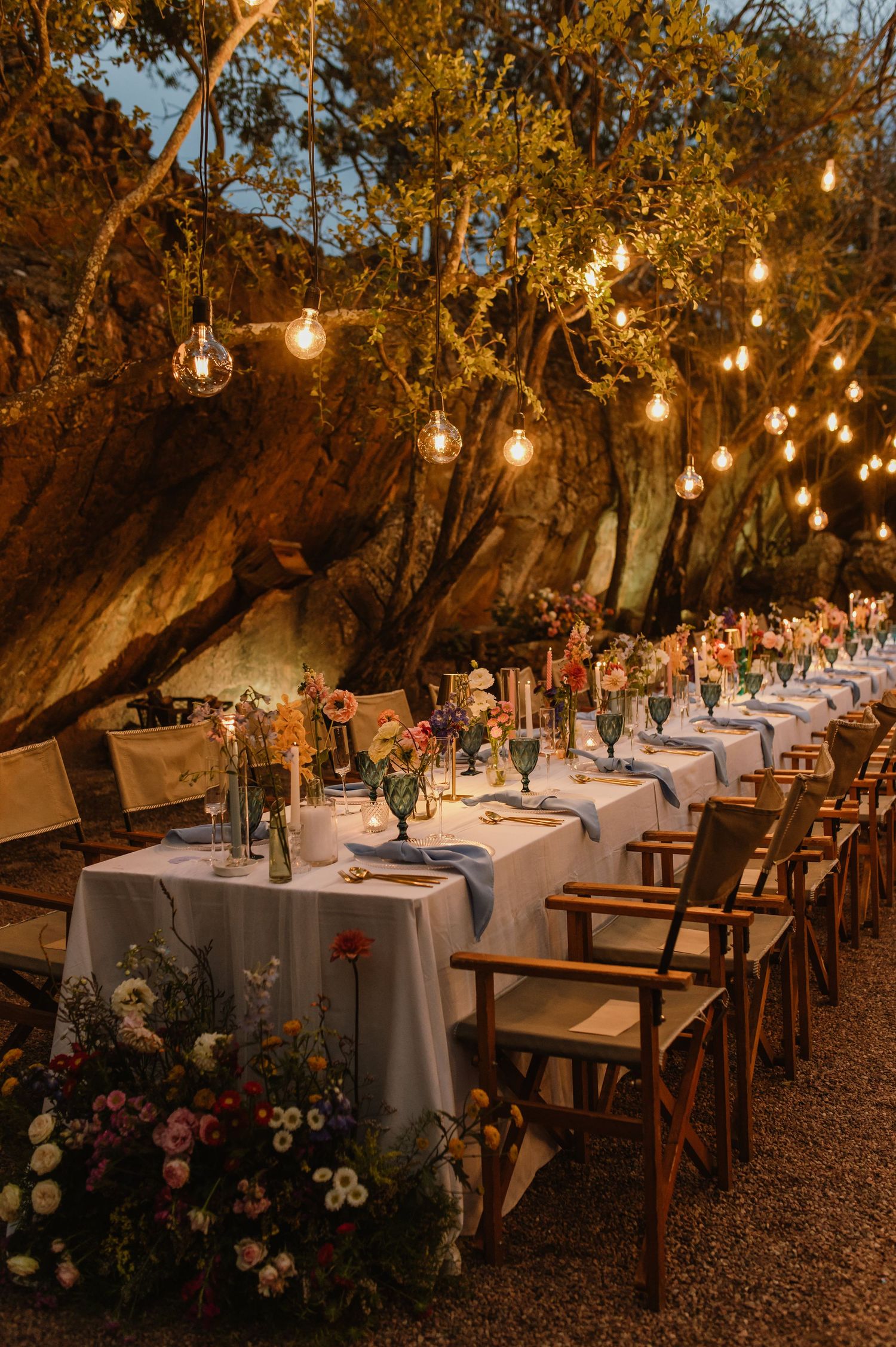 Romantic outdoor wedding reception with long tables, colorful florals, and Edison bulb string lights.