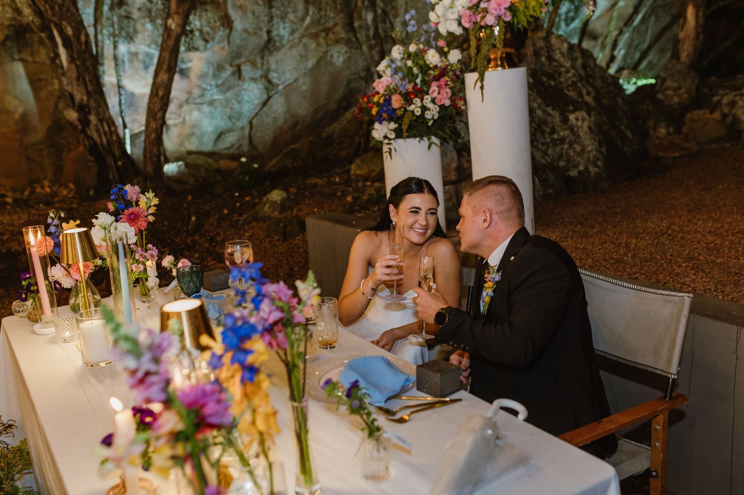 Bride and groom sharing a toast and laughing at sweetheart table in romantic cave wedding venue.