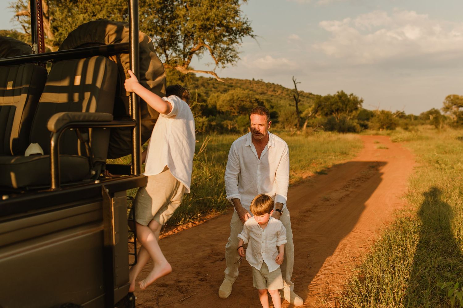 Family enjoying a safari game drive on a dirt road at golden hour in an African savanna landscape.