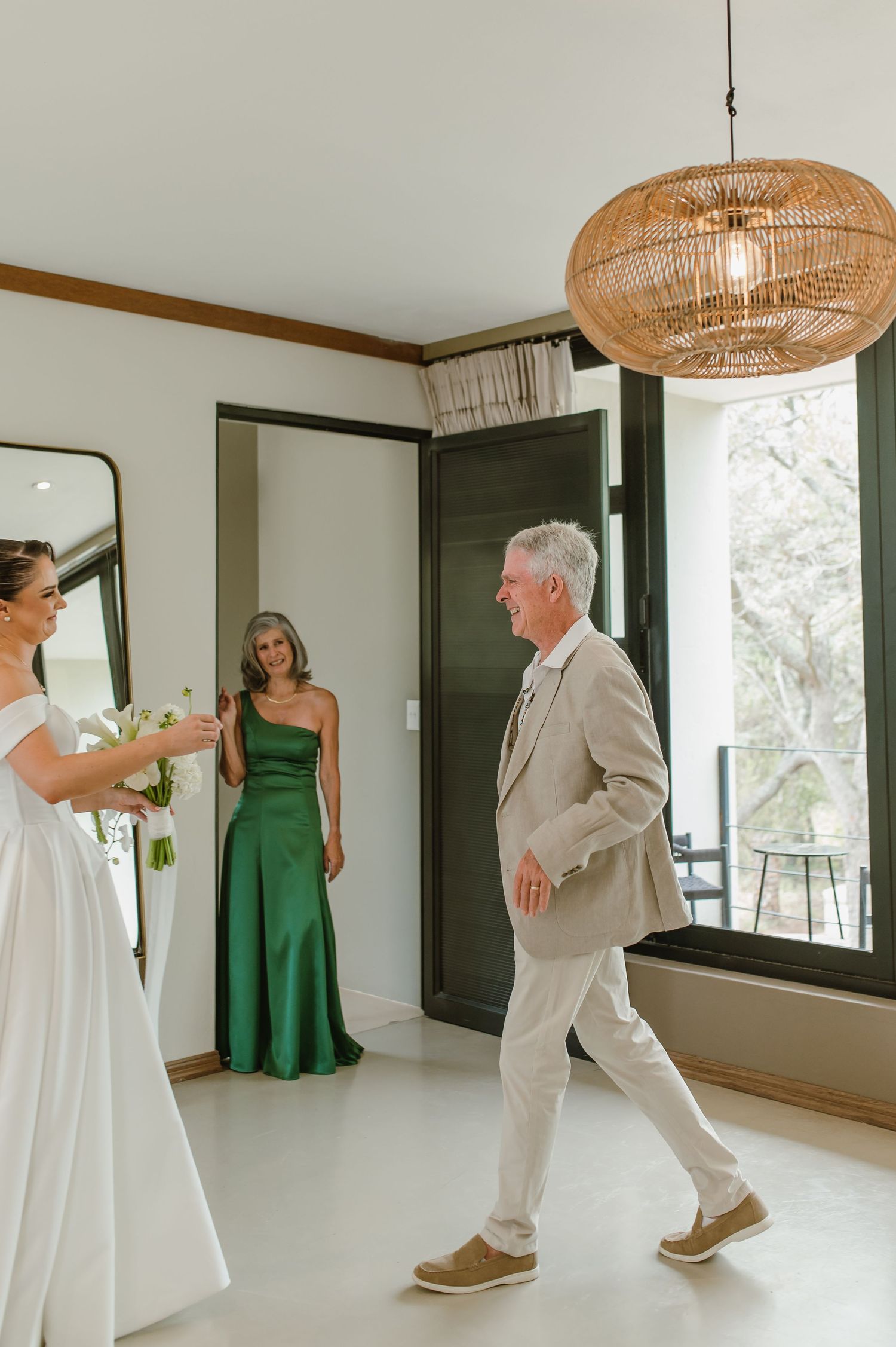 First look wedding moment in a bright modern space with rattan lighting and mirrors.