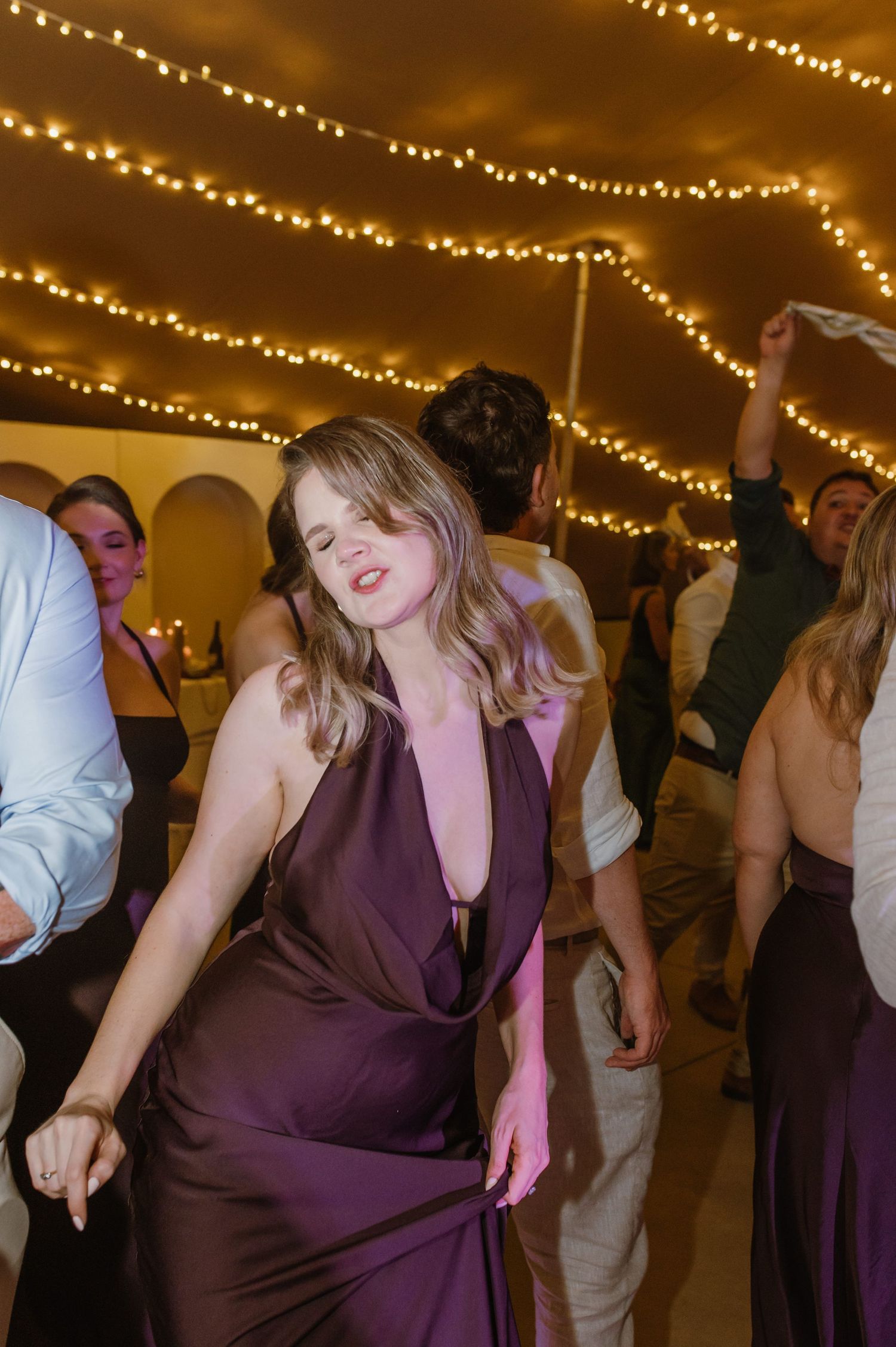 Wedding guests dancing under golden string lights at an evening reception celebration.