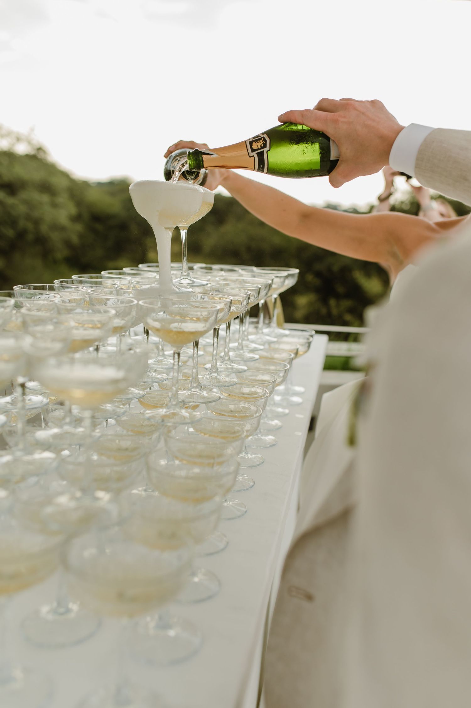 Multiple champagne glasses being filled at an elegant outdoor event.