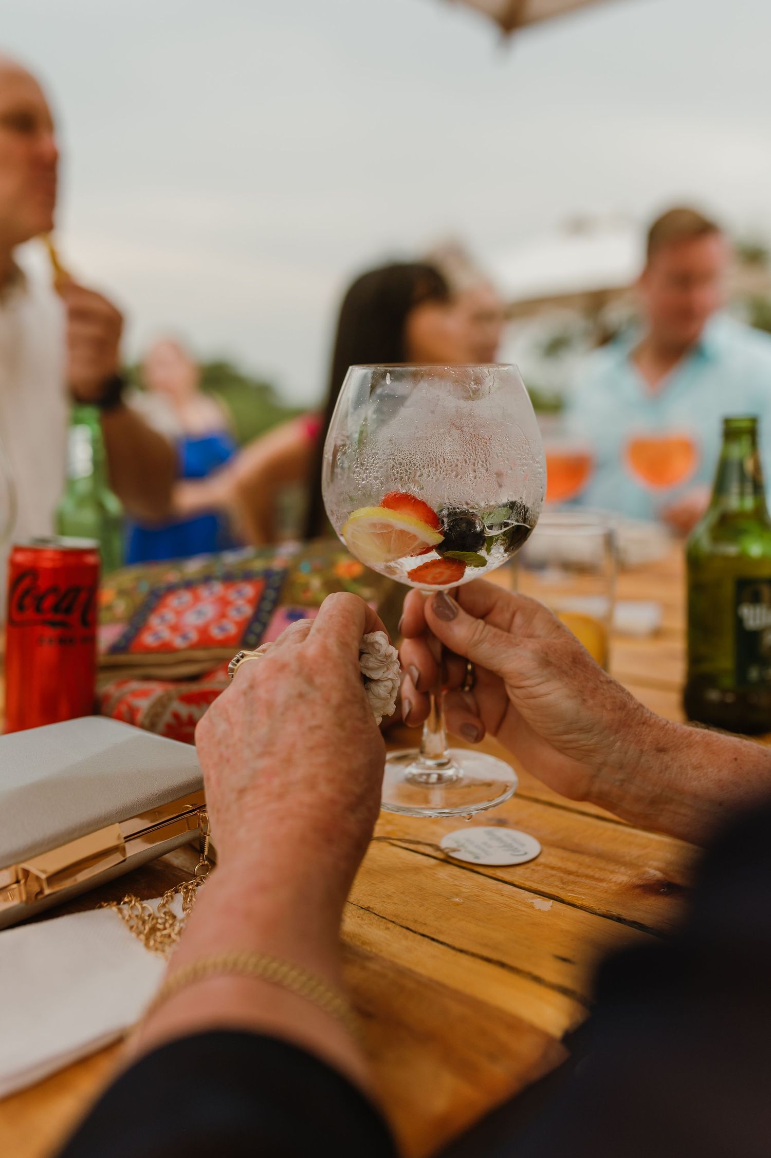 Close-up of hands holding wine glasses during a toast at an outdoor wooden table.