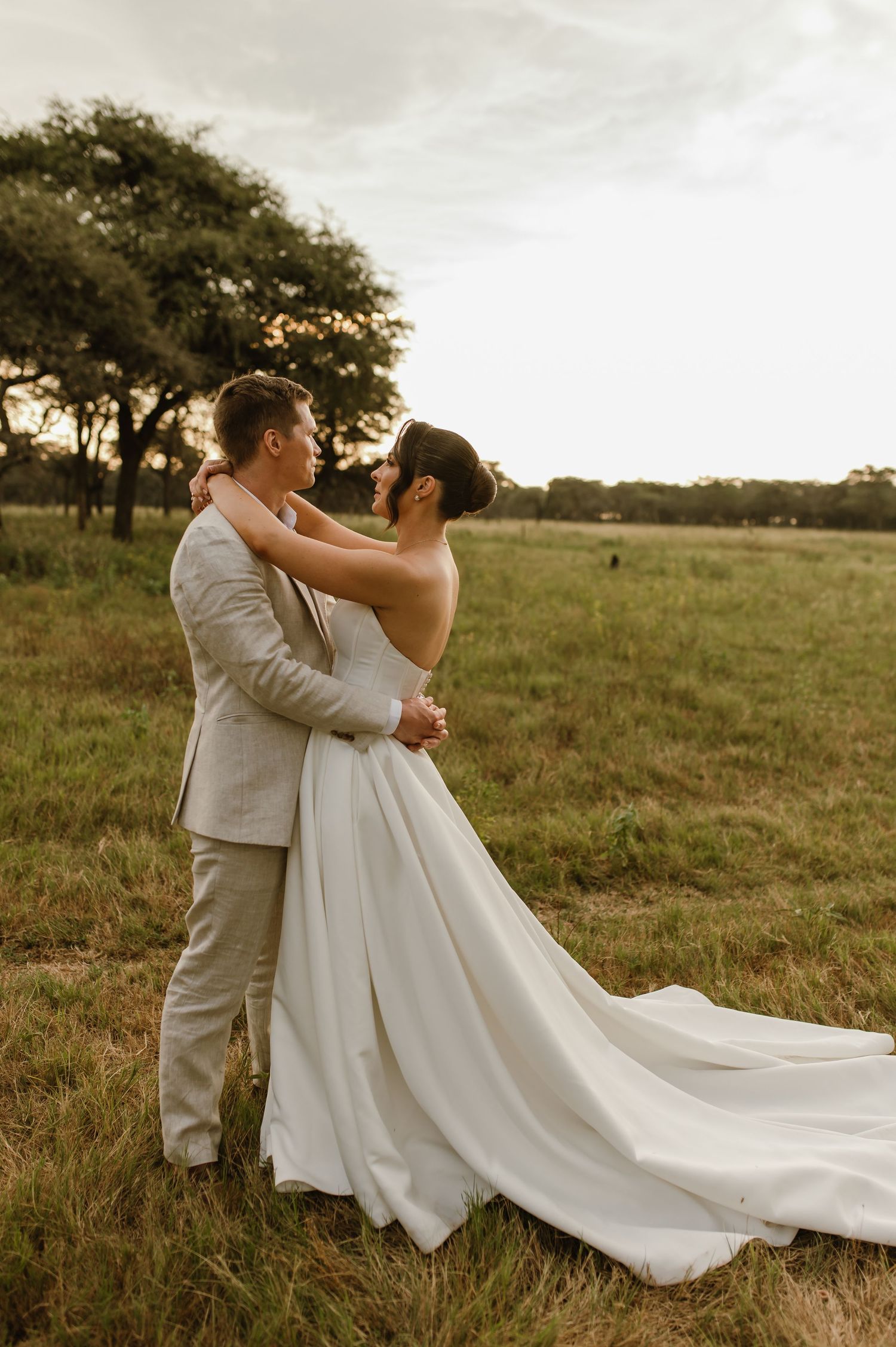 A romantic wedding couple dances together in an open field with flowing white dress.