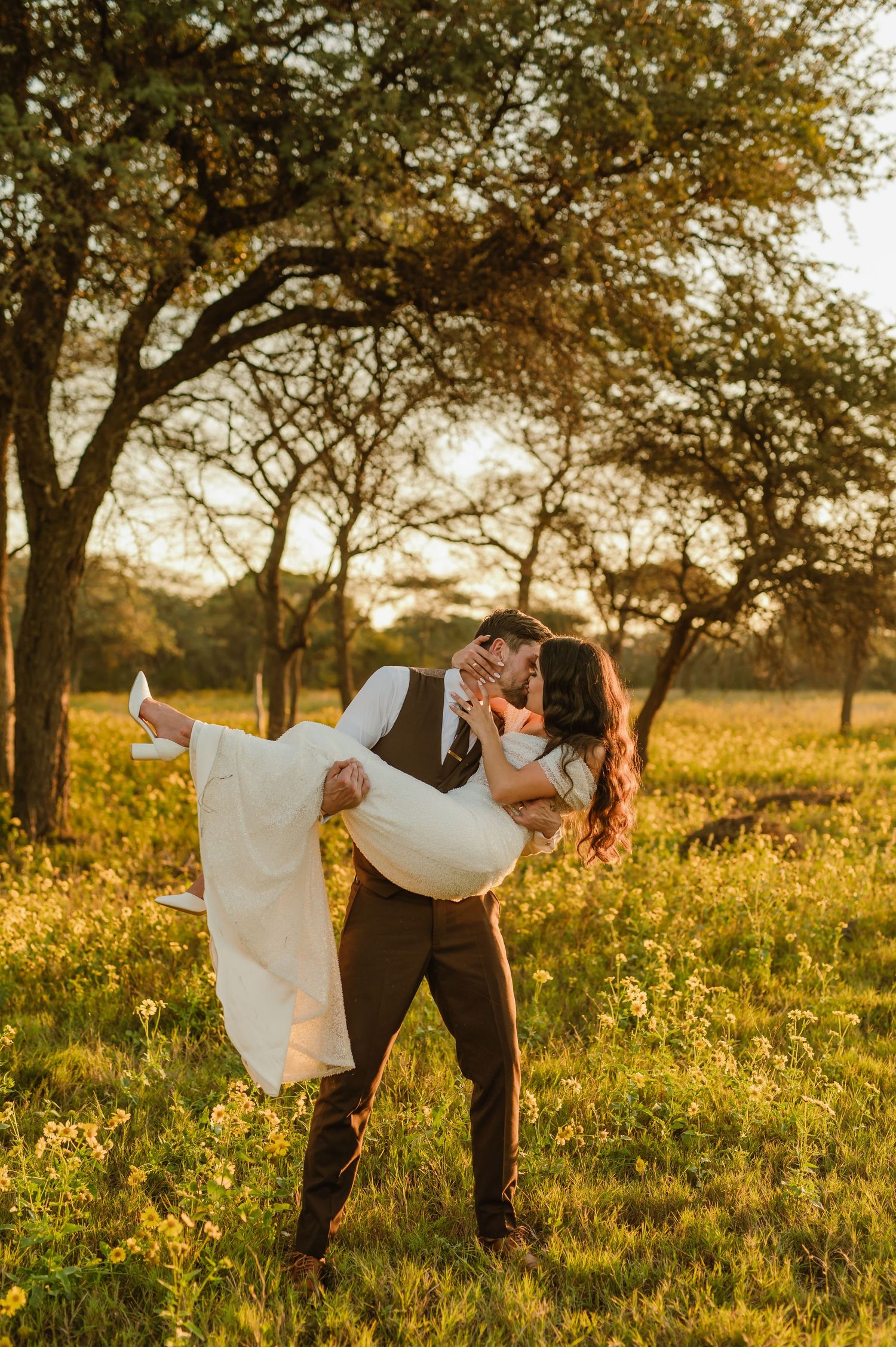 A romantic couple dances in a sunlit meadow with wildflowers during golden hour at sunset.