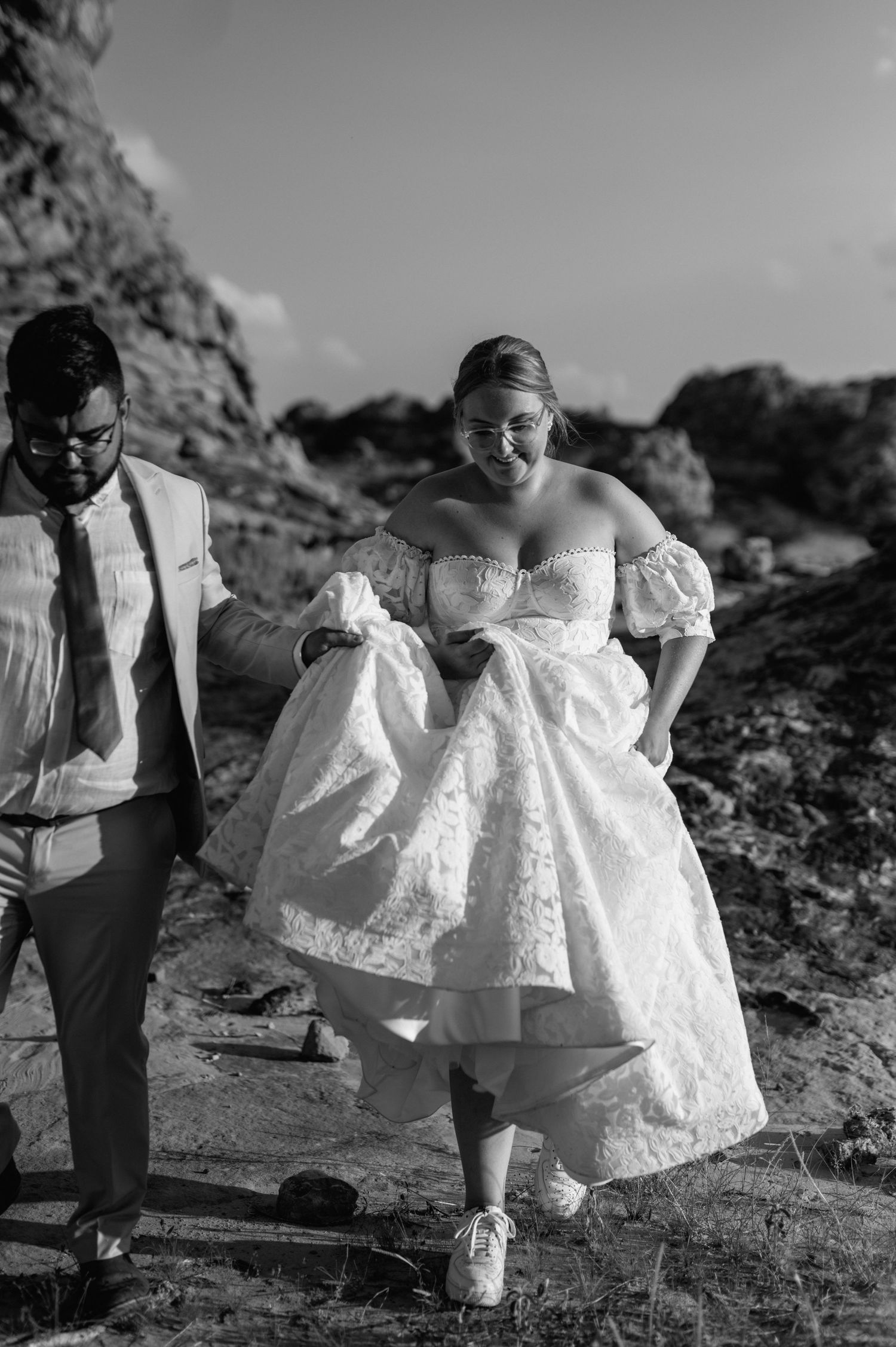 Black and white photo series showing someone in a flowing white lace dress walking across rocky terrain.