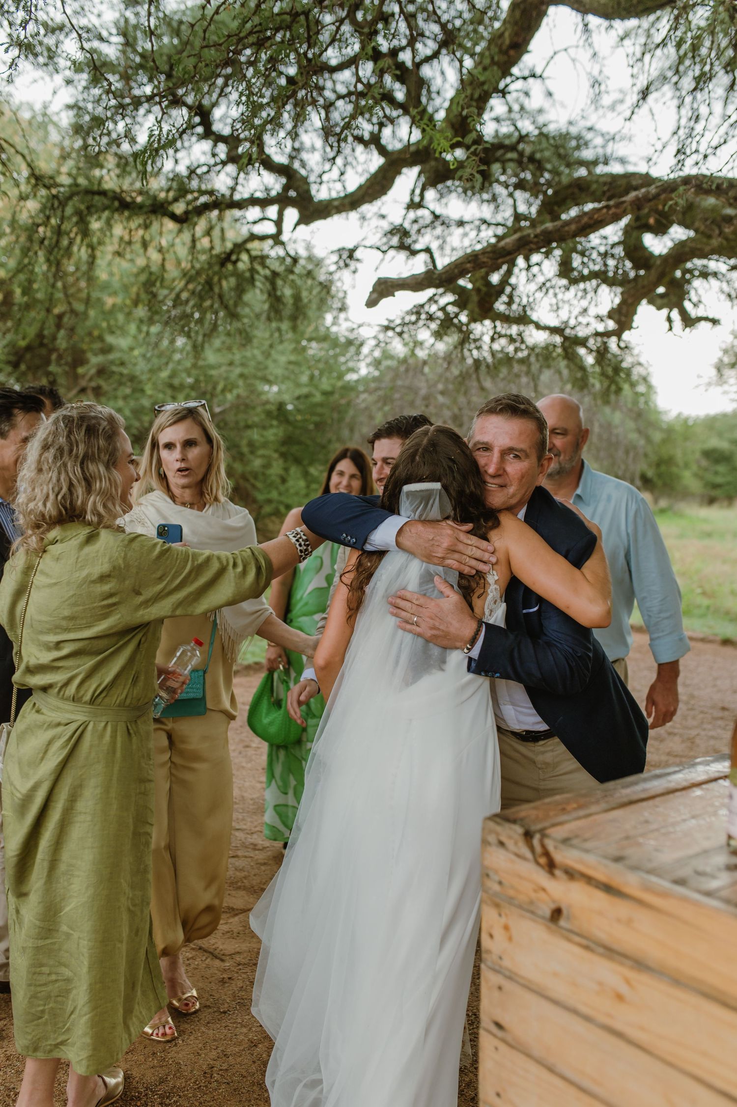 Wedding celebration with guests embracing and sharing emotional moments outdoors.