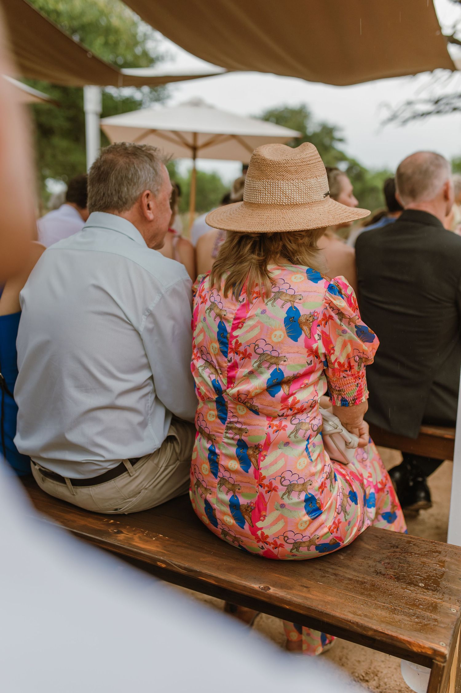 Wedding guests sit on rustic wooden benches at an outdoor ceremony venue.
