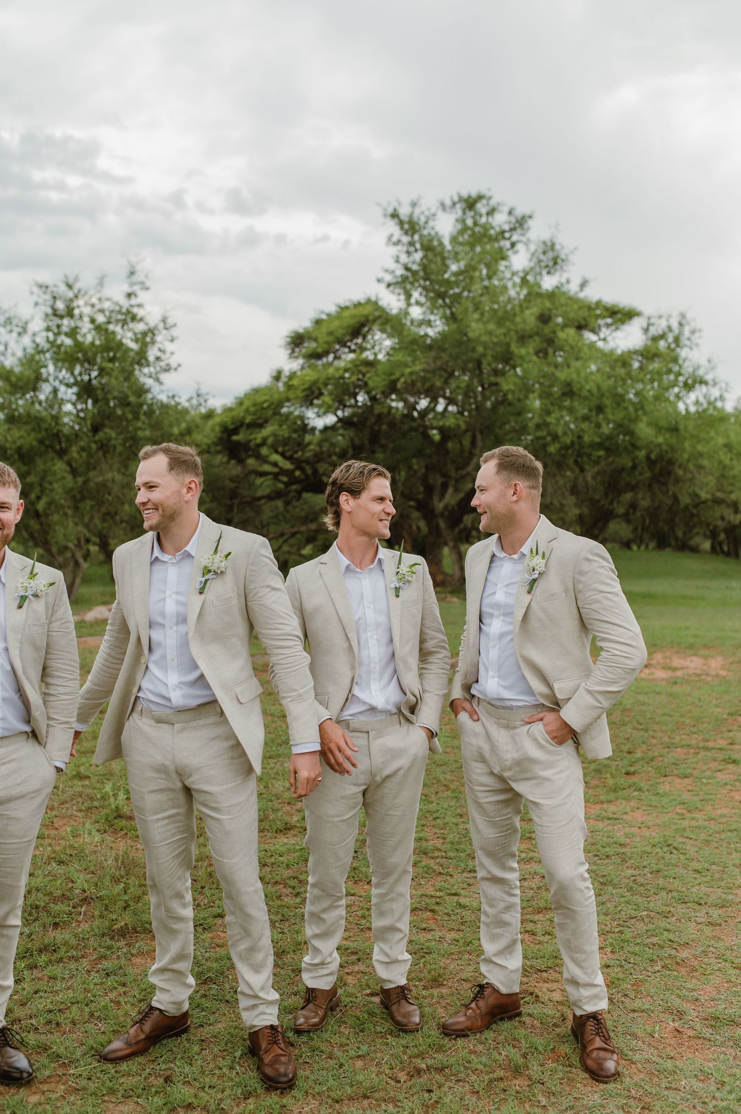 Groomsmen in light beige suits laughing together in casual group pose.