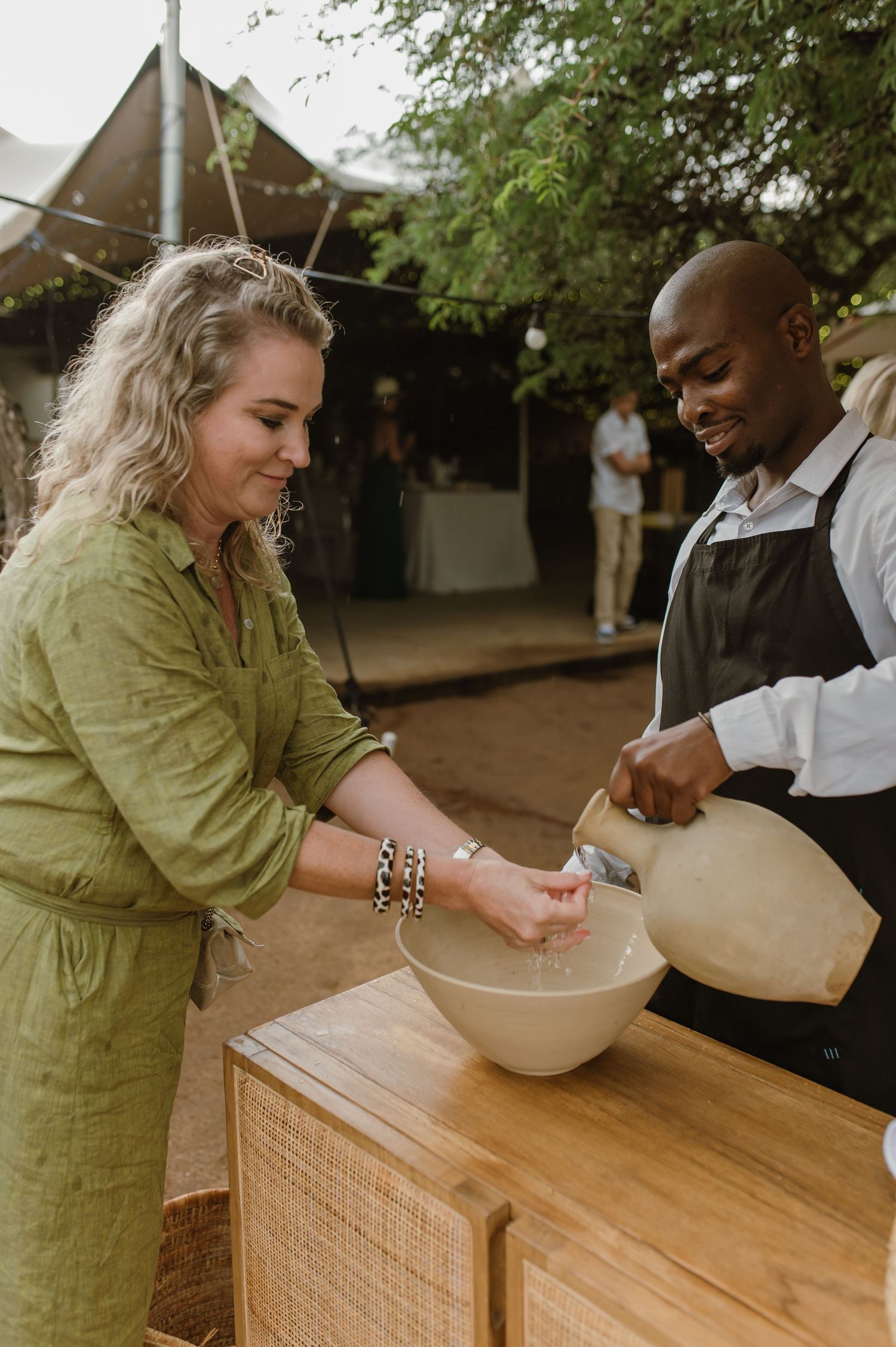 Two people preparing drinks at a wooden bar station during an outdoor event.
