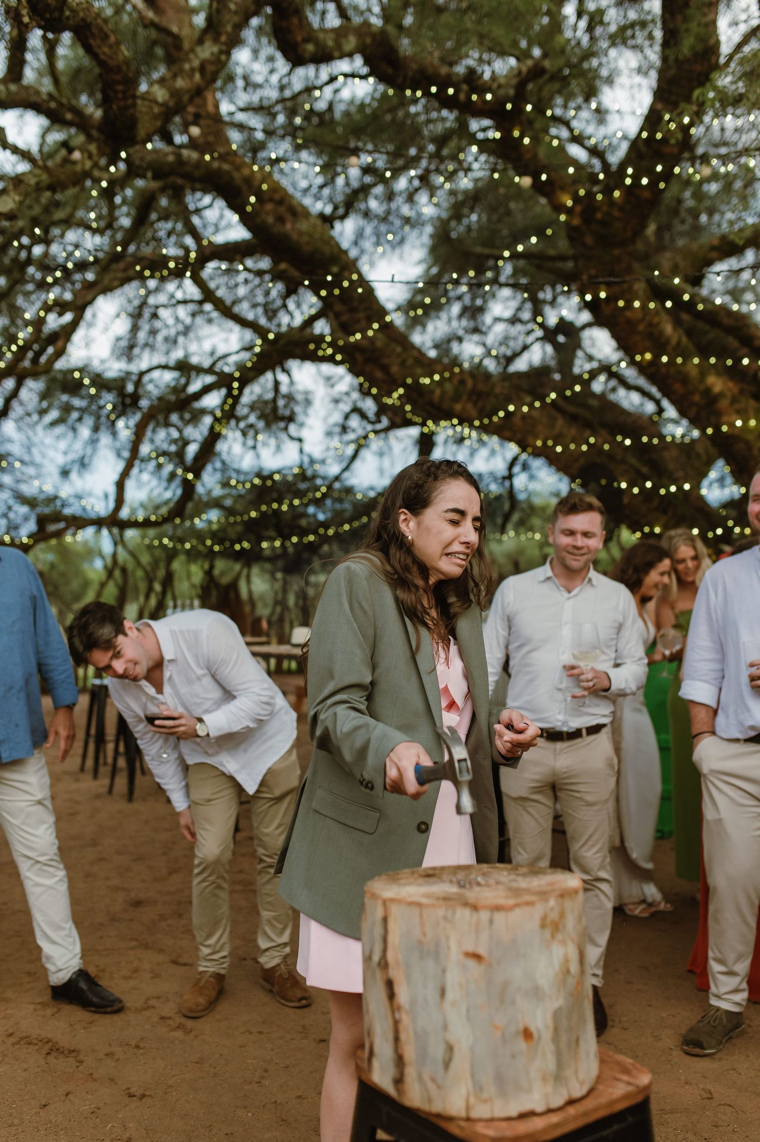 Wedding guests gathered around rustic barrels under string lights at an outdoor reception.