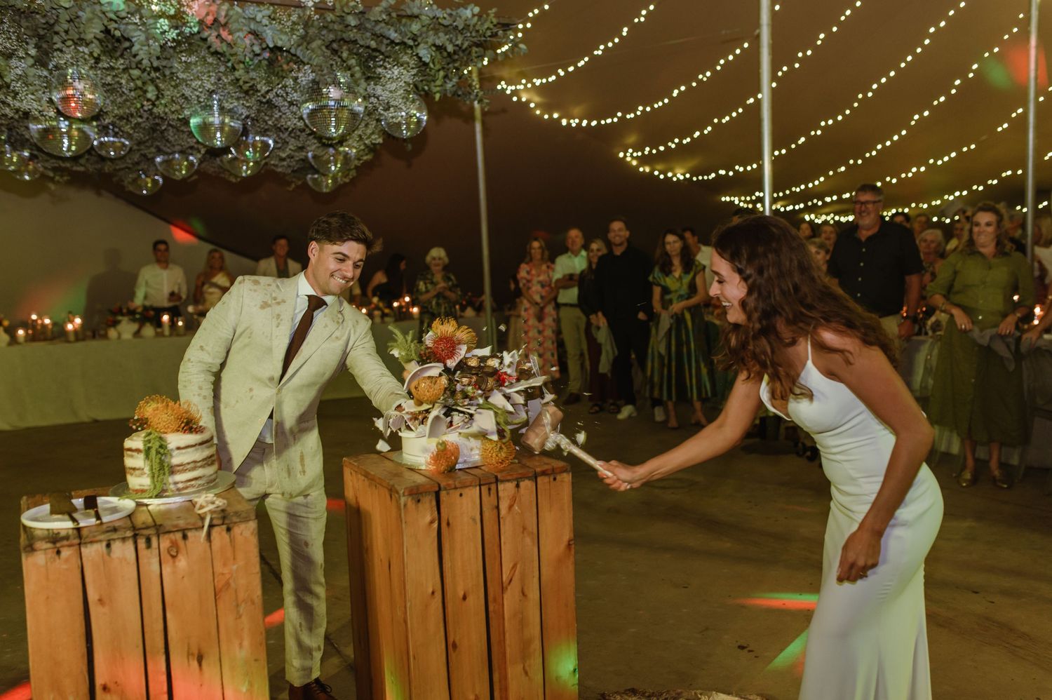 Couples dance near rustic wooden decor under string lights at outdoor wedding reception.