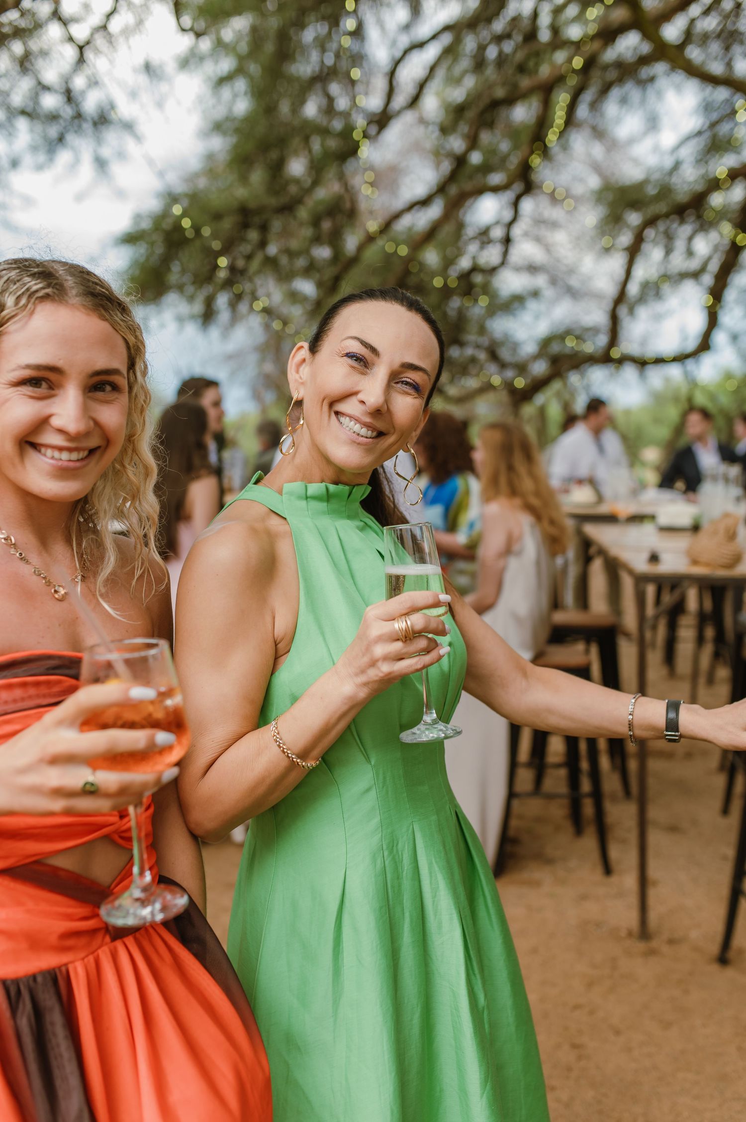 Bridesmaids in coral and mint green dresses holding cocktails at an outdoor reception.