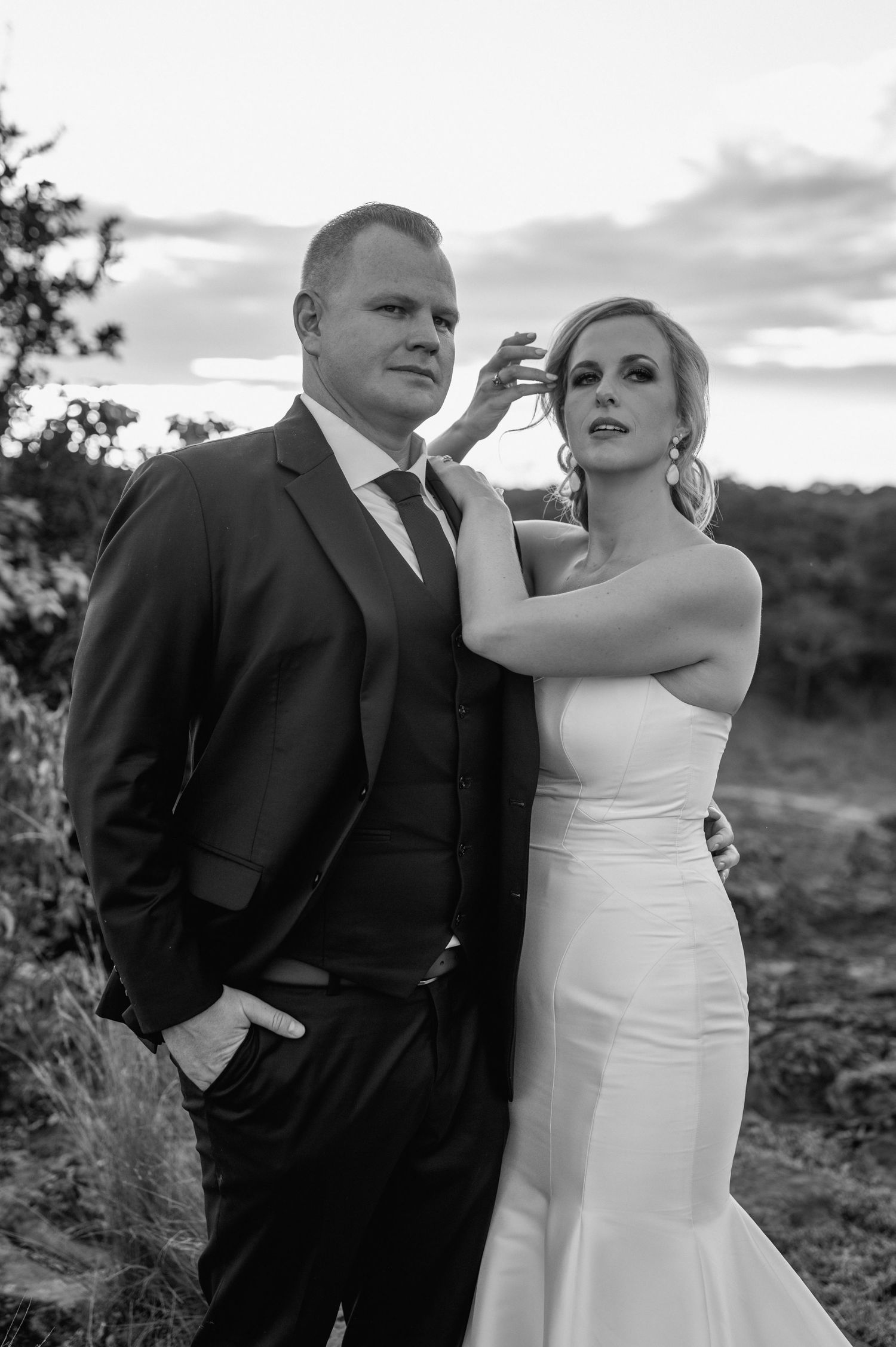 Playful wedding couple interacts on rocky terrain during sunset photo session.