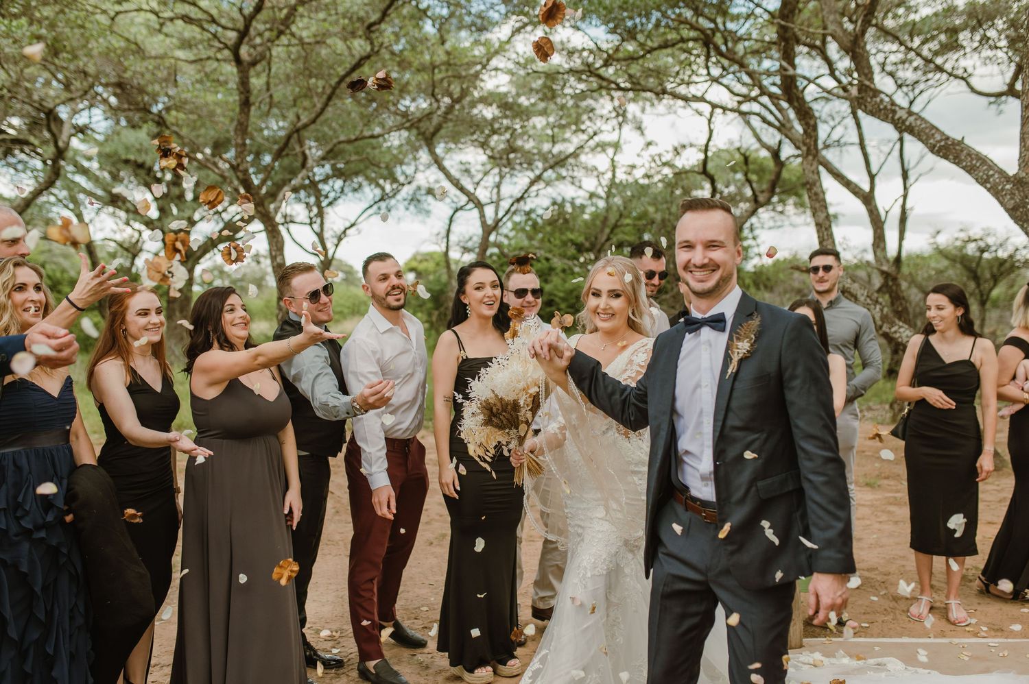 Wedding party and guests celebrate during an outdoor ceremony with natural backdrop.