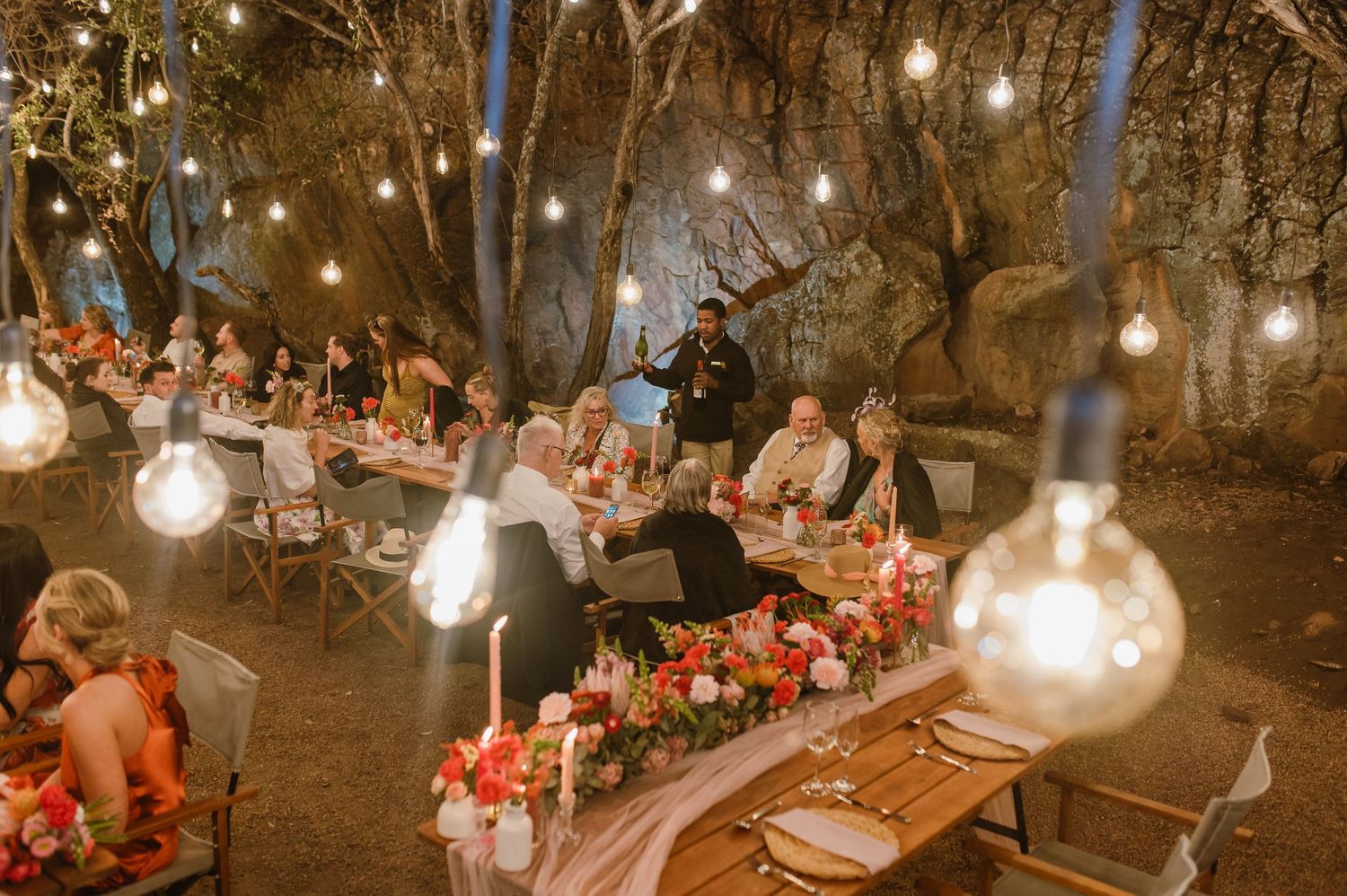 Panoramic view of an outdoor wedding reception with string lights and rustic wooden tables.