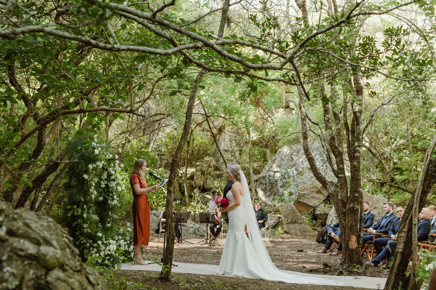 Forest wedding ceremony setup with guests seated among natural greenery.