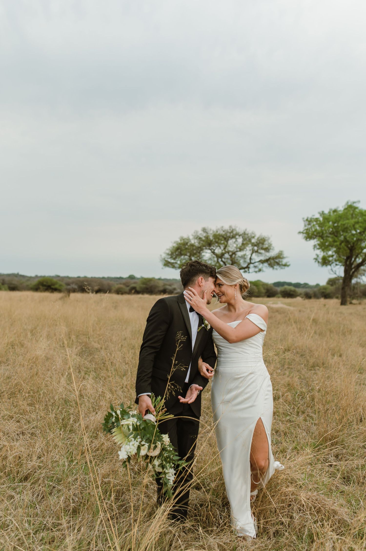 A couple in wedding attire shares an intimate moment in a golden grass field.