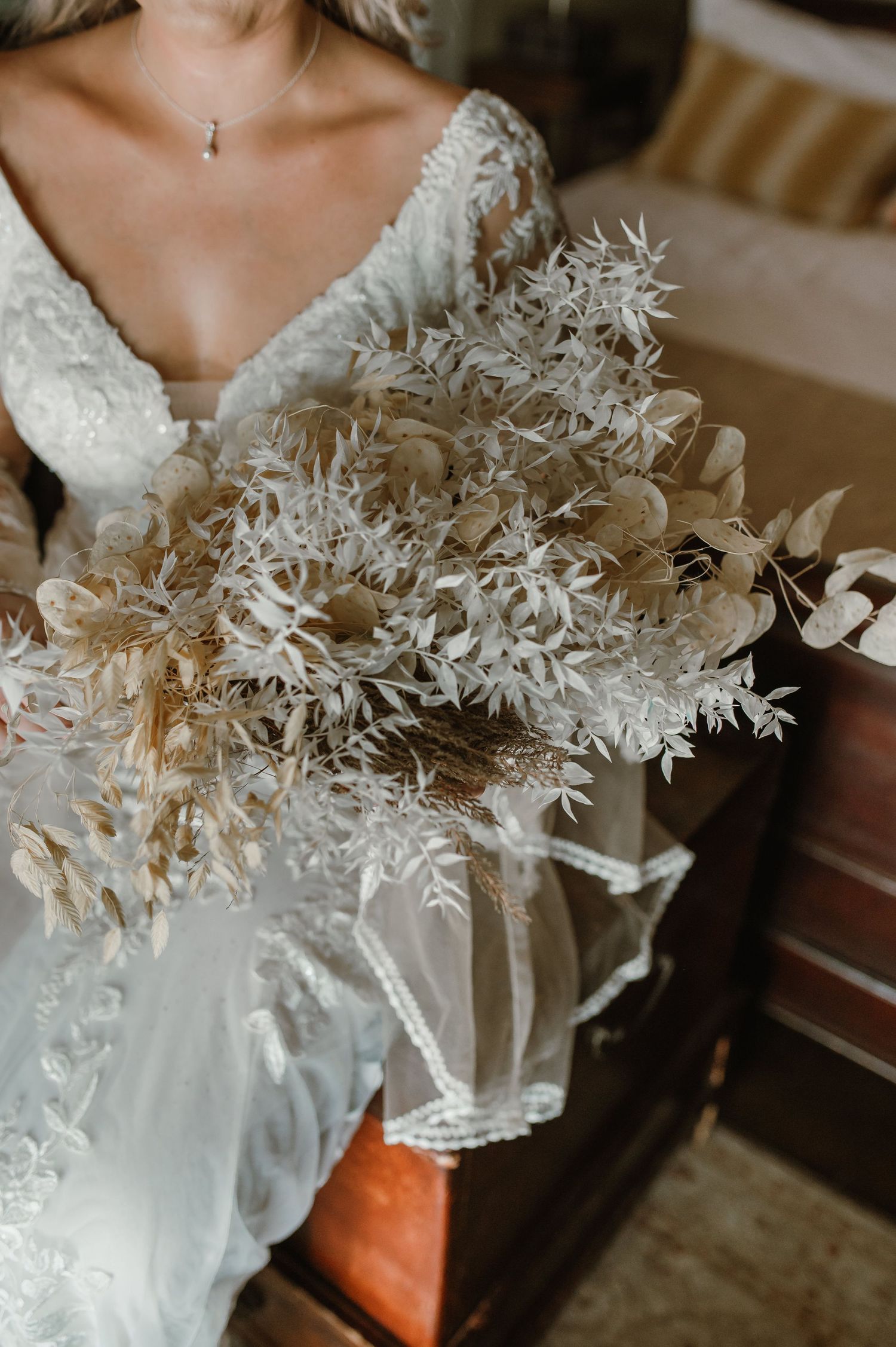 Close-up detail of dried floral elements against a white lace wedding dress.
