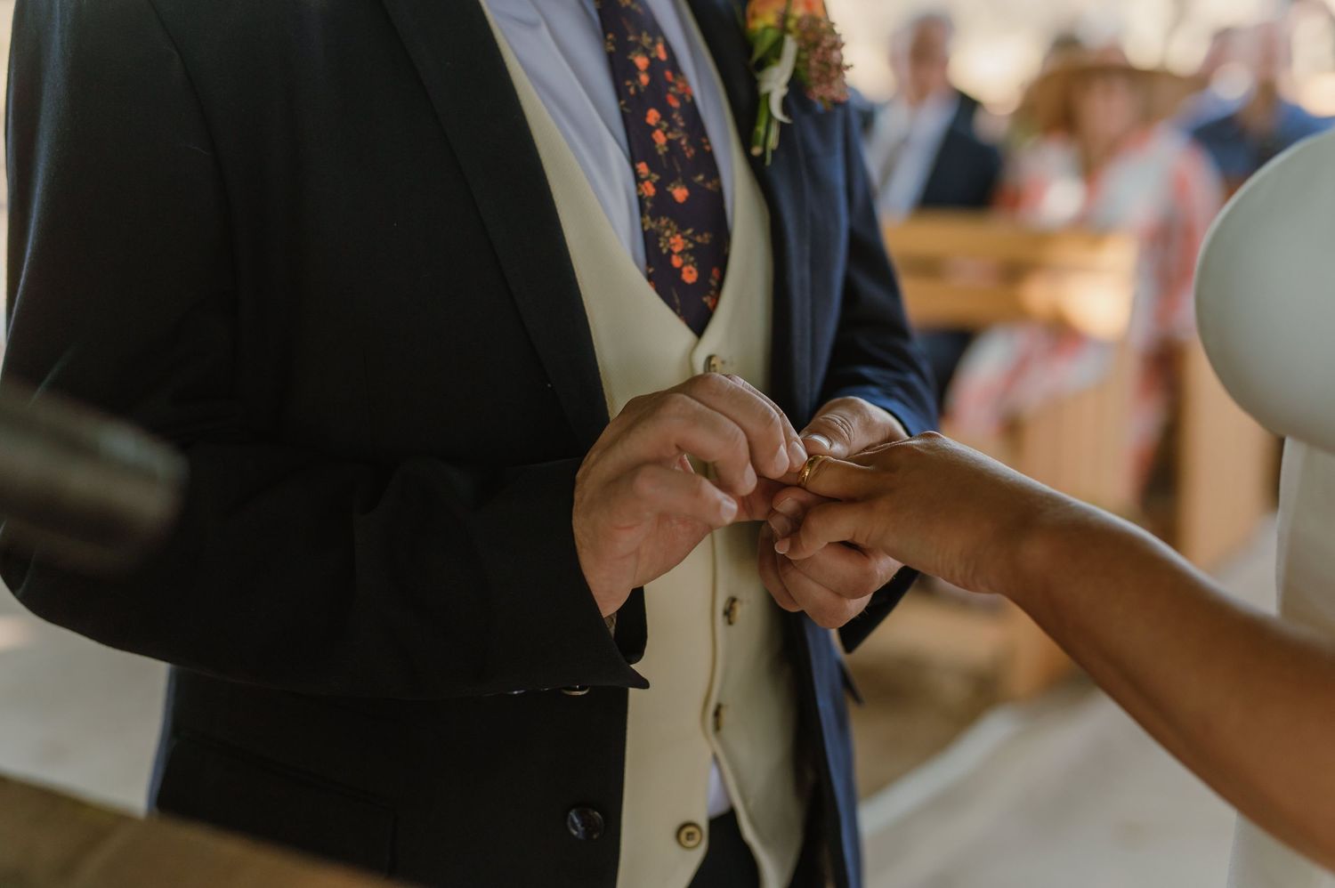 Close-up of hands during wedding ring exchange ceremony outdoors.