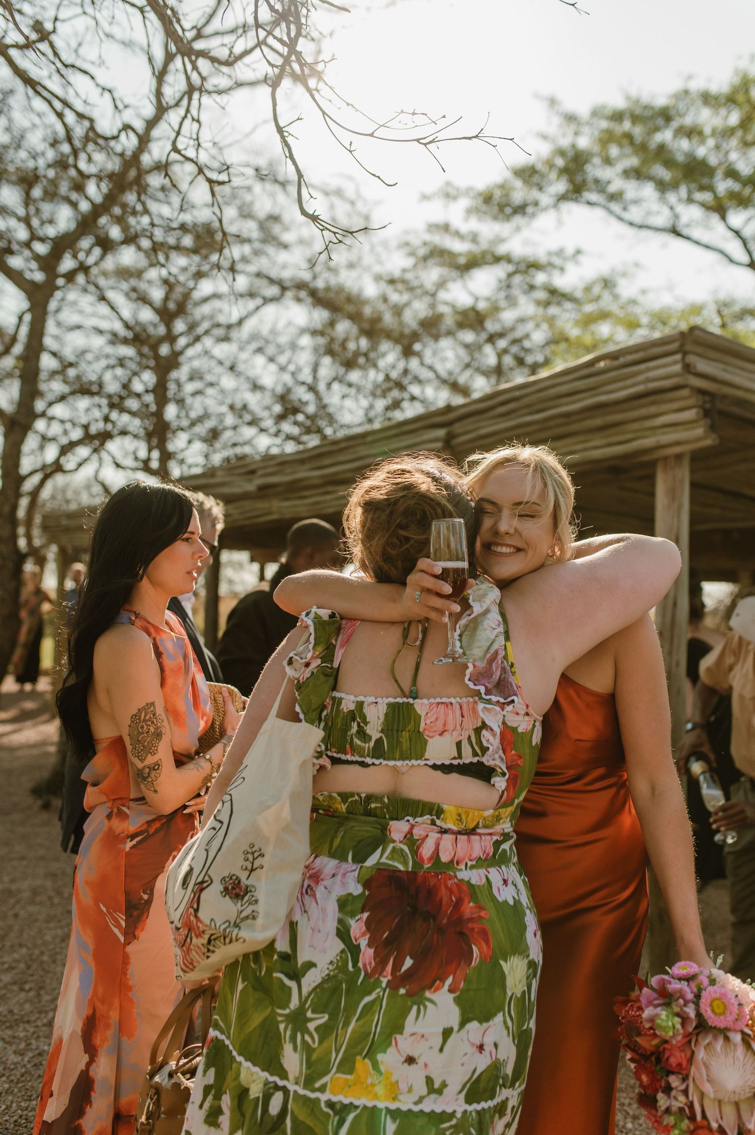 Wedding party in coral and floral dresses laughing together outdoors.
