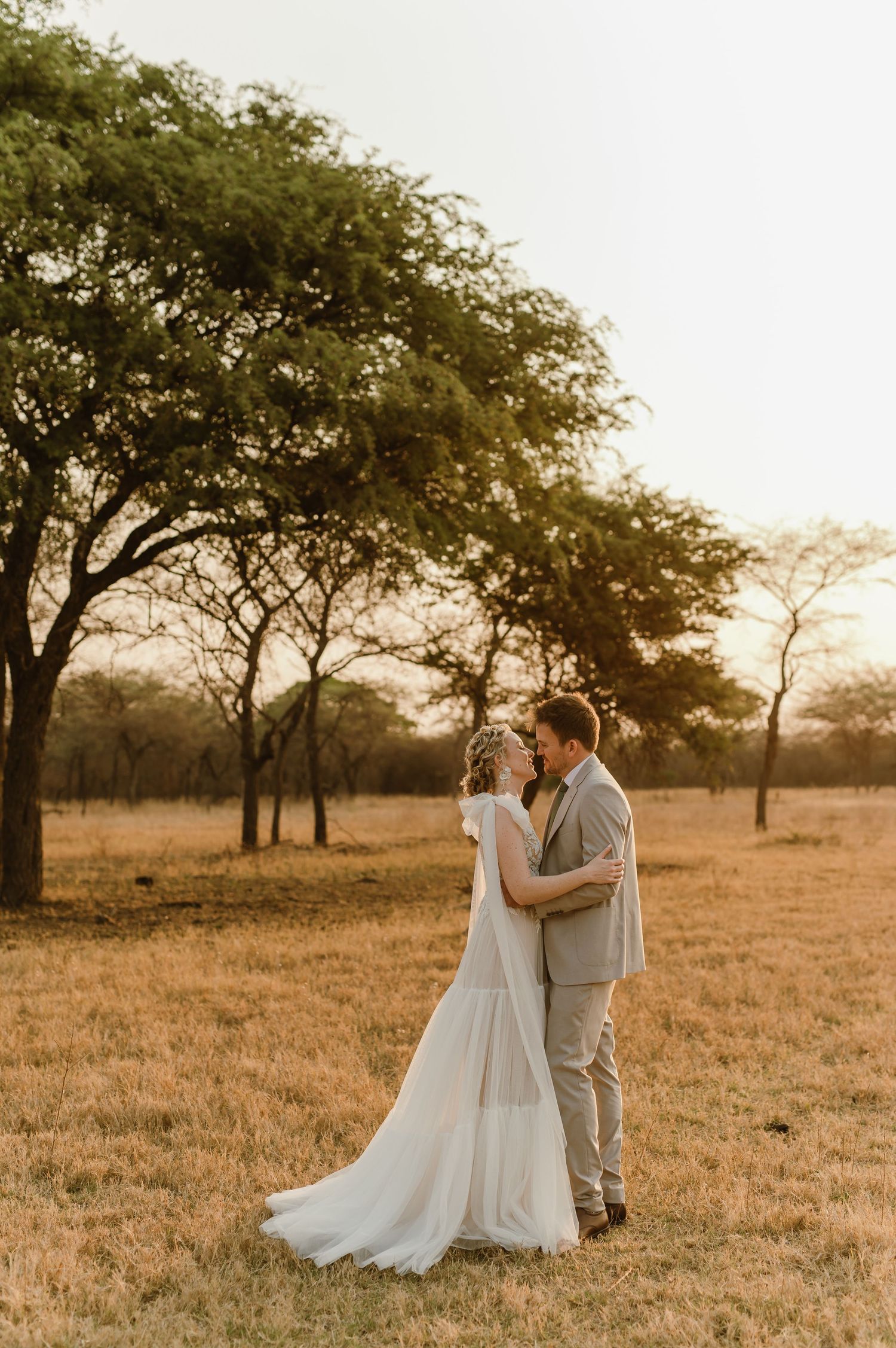 Romantic wedding portrait under acacia trees in African savanna during golden hour.