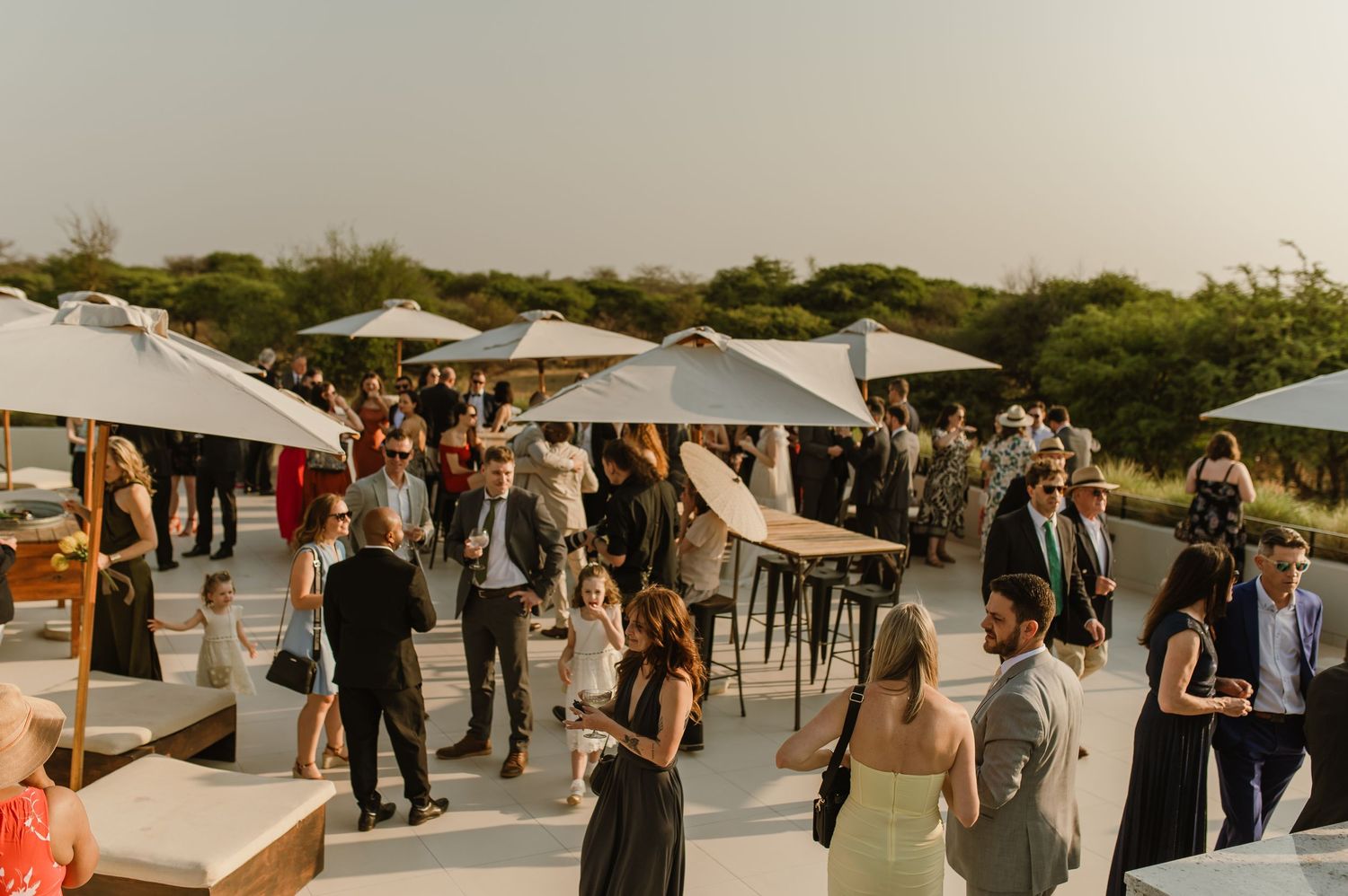 Panoramic view of an outdoor wedding reception with umbrellas and mingling guests.