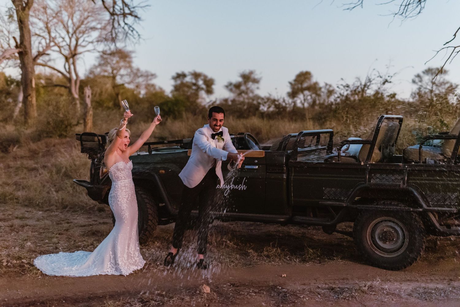 Vintage Land Rover vehicles parked along a dirt path serve as backdrop for an outdoor wedding shoot.