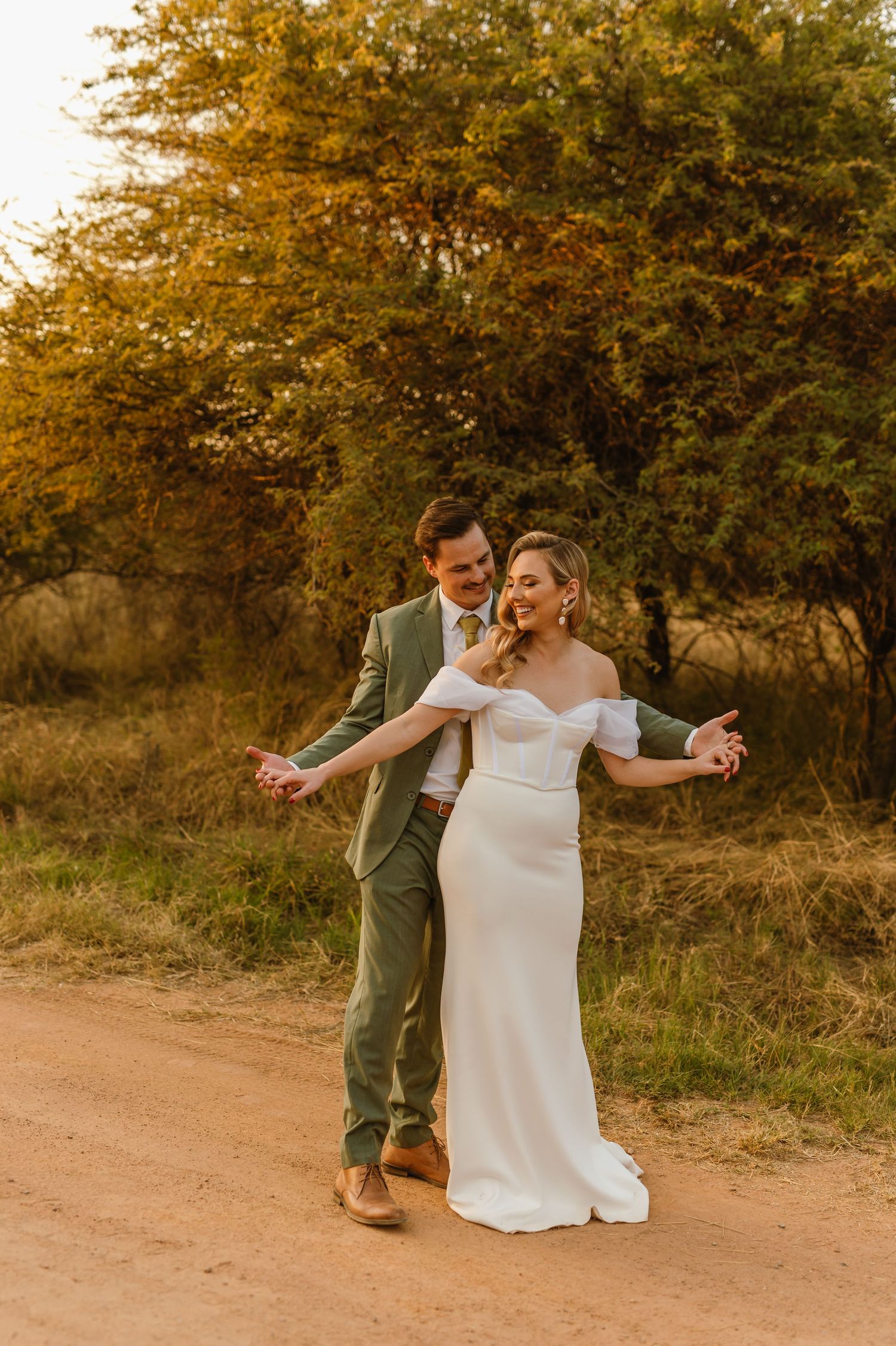Couple dancing together on a dirt path surrounded by autumn trees during golden hour.
